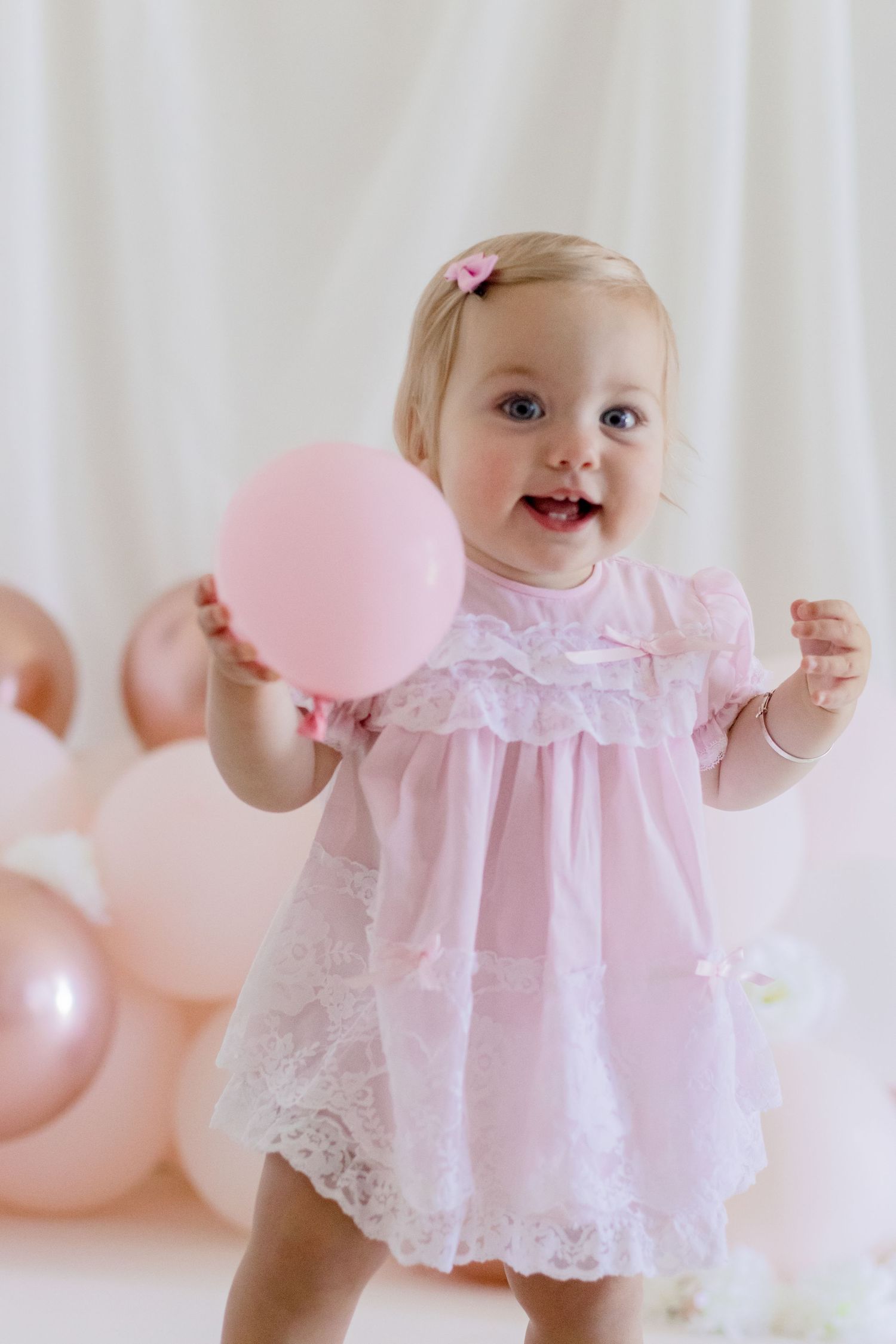 Excited baby in pink lace dress playing with balloon during photo shoot.
