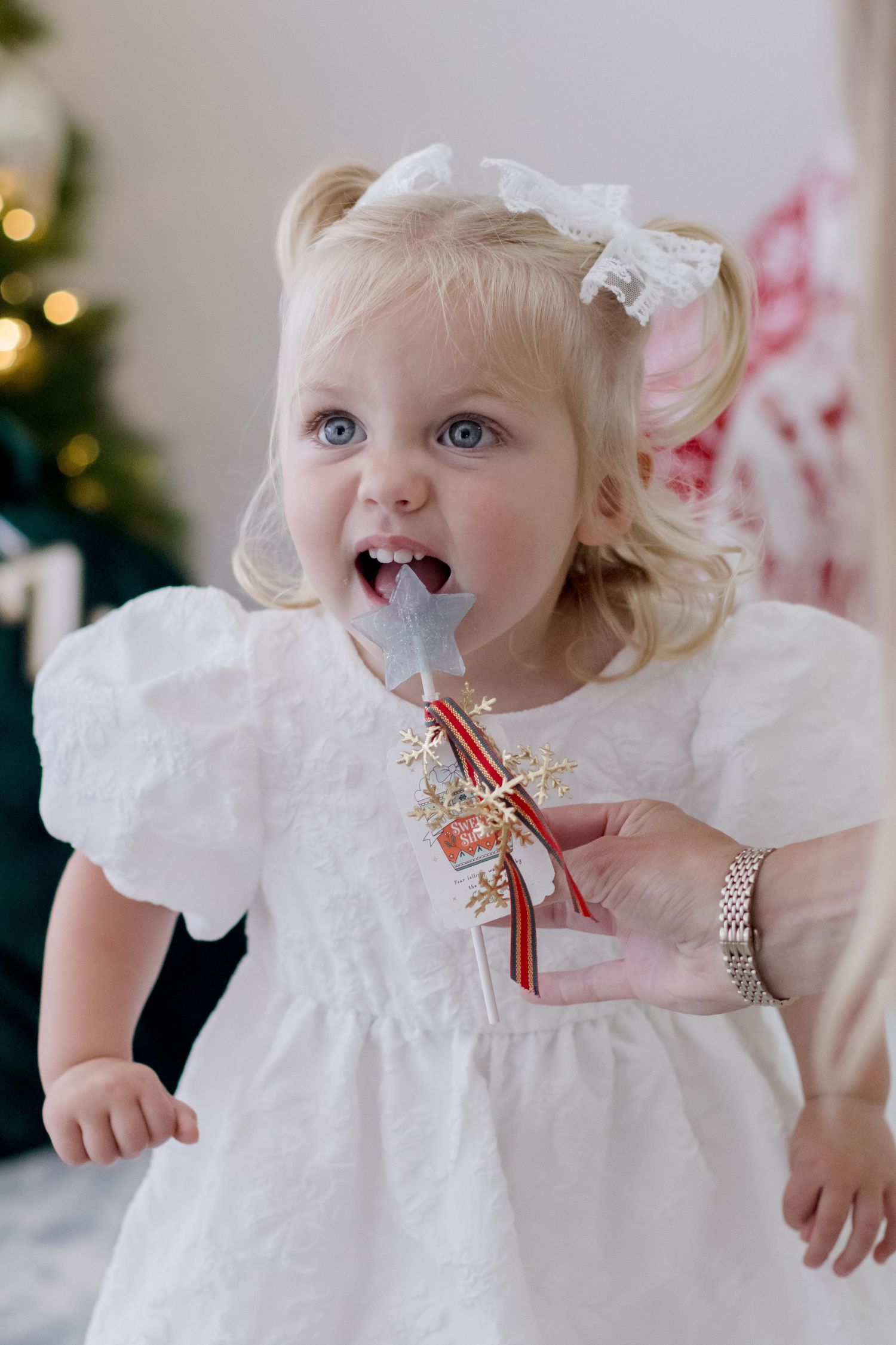 White lace dress with festive red ribbon details shown in multiple close-up views against holiday lights.