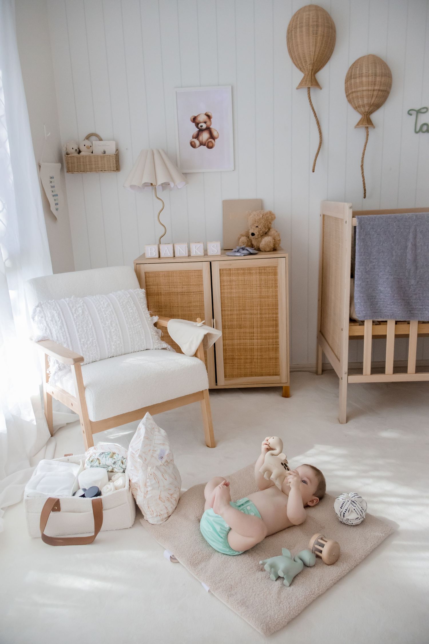 Modern neutral nursery with wooden furniture, balloon decor, and baby essentials on a light carpet.