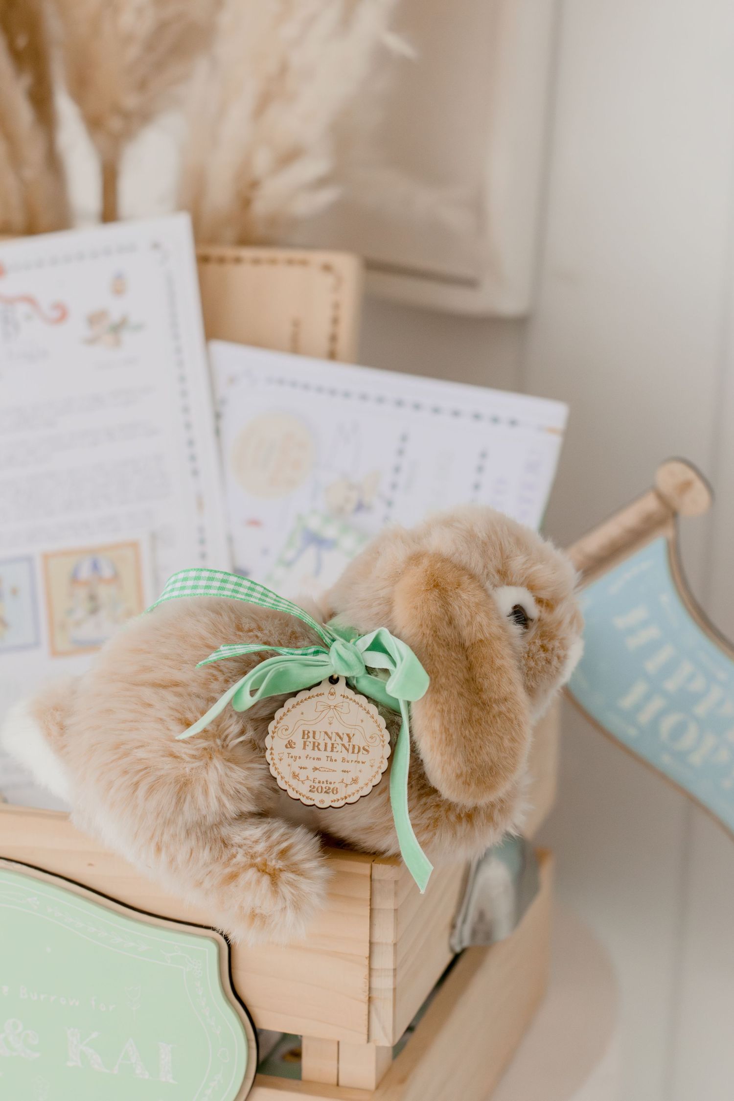 Fluffy bunny stuffed animal with green ribbon in a wooden crate with Easter cards and decorations.