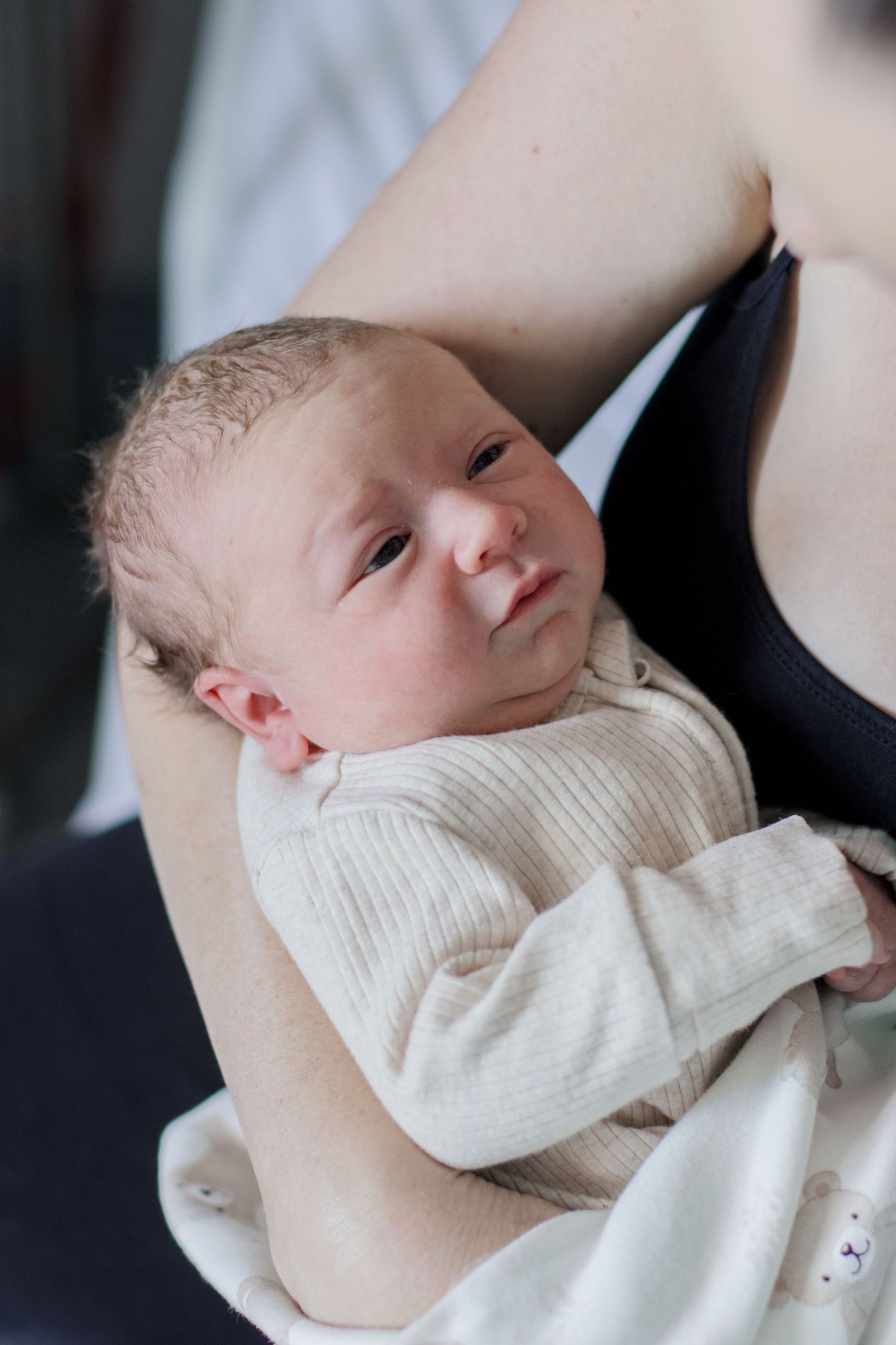 Tiny newborn wearing white sweater rests against caregiver in dark top.
