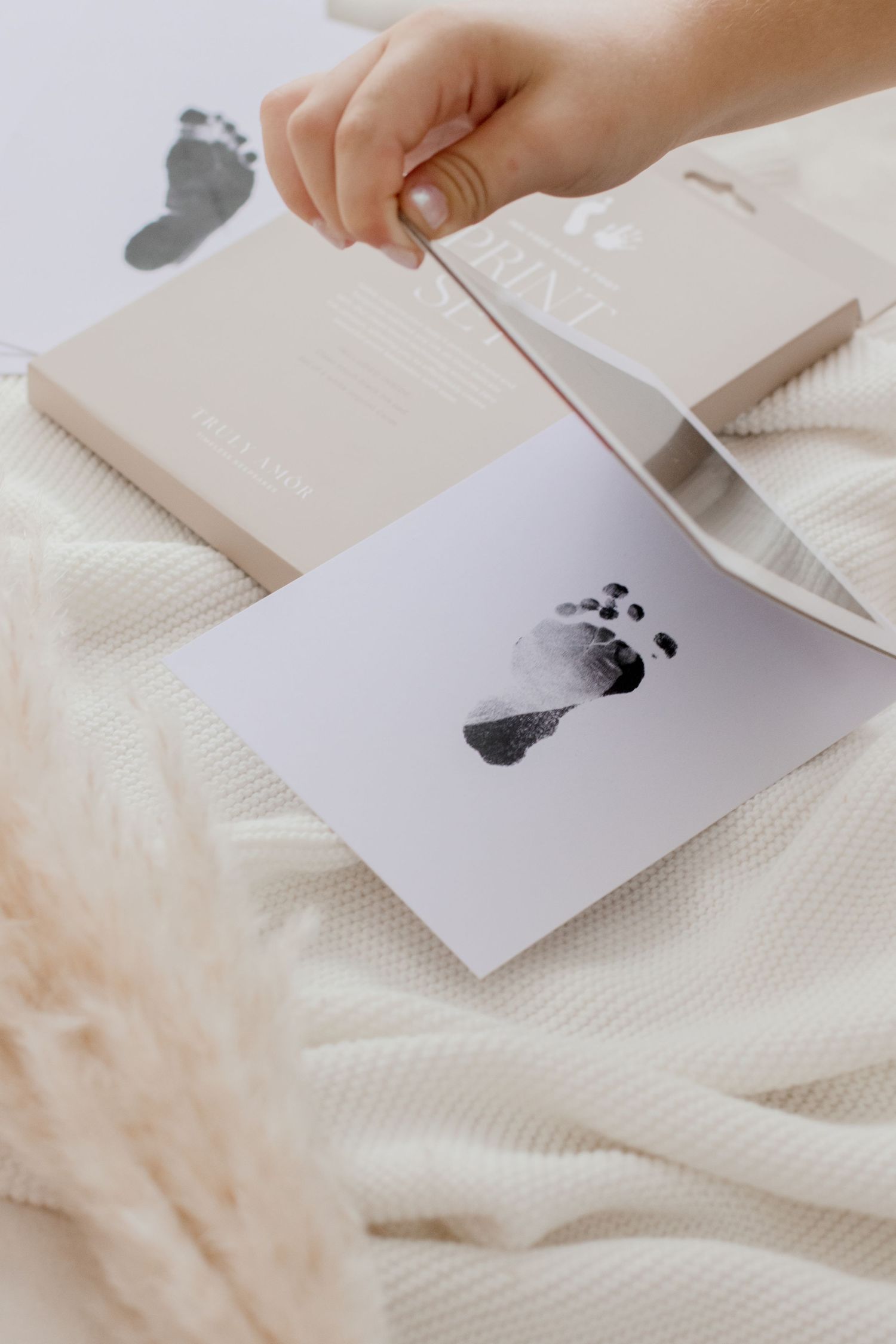 Hand placing black ink on white paper creating artistic print patterns on a soft textured background.