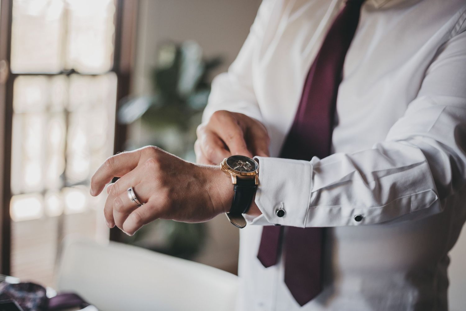 A person in business attire adjusts their watch and sleeve cuff while wearing a burgundy tie.