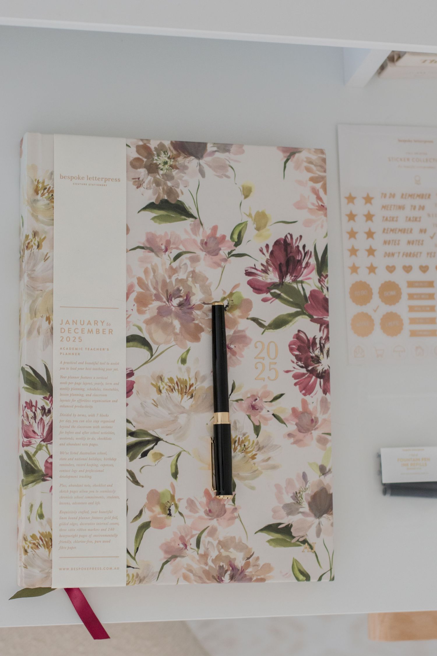 Floral patterned planner with gold accents and fountain pen on white surface.
