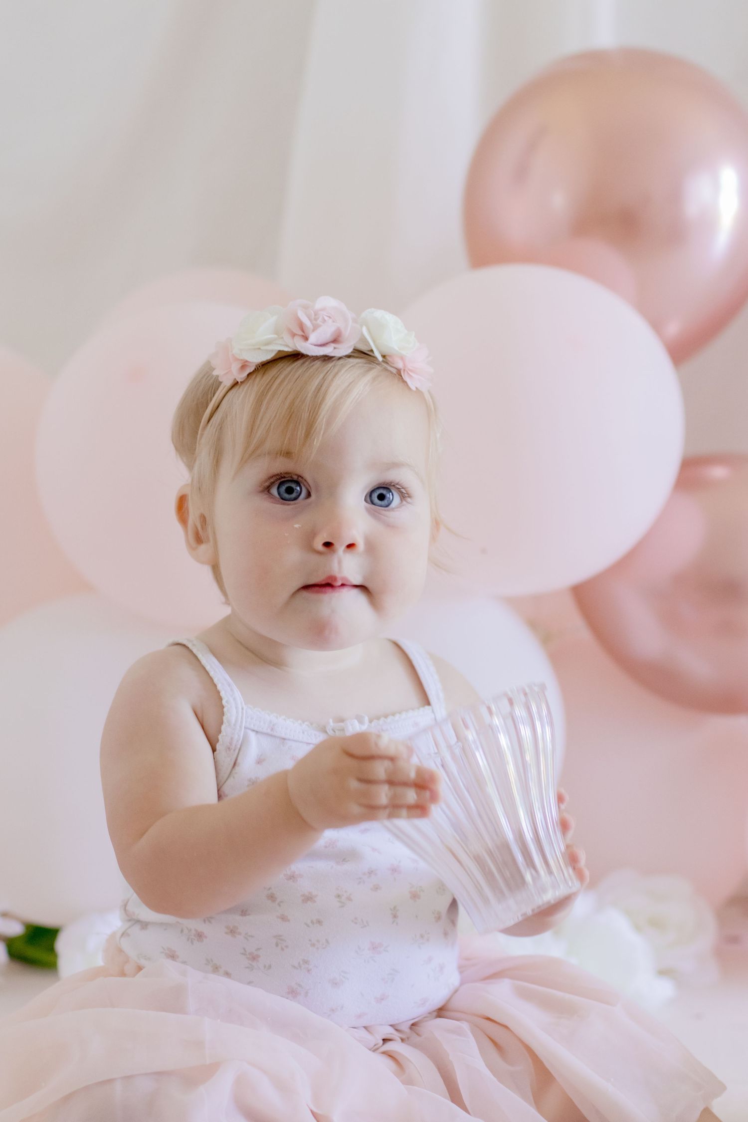 Elegant first birthday portrait with pink balloons and floral crown.