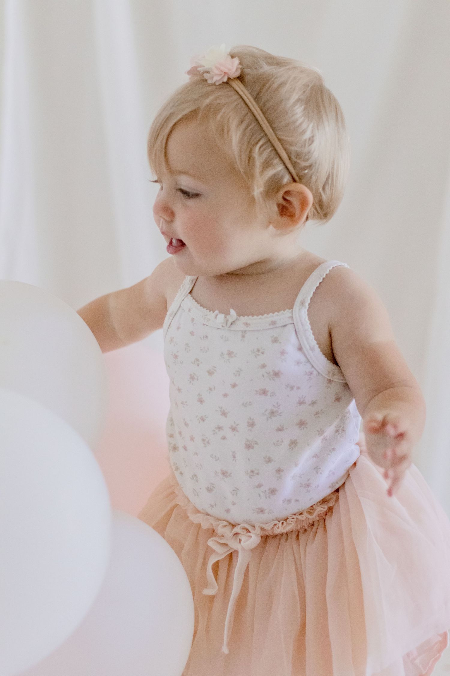 Young child in pink tutu dress with floral headband against white backdrop.