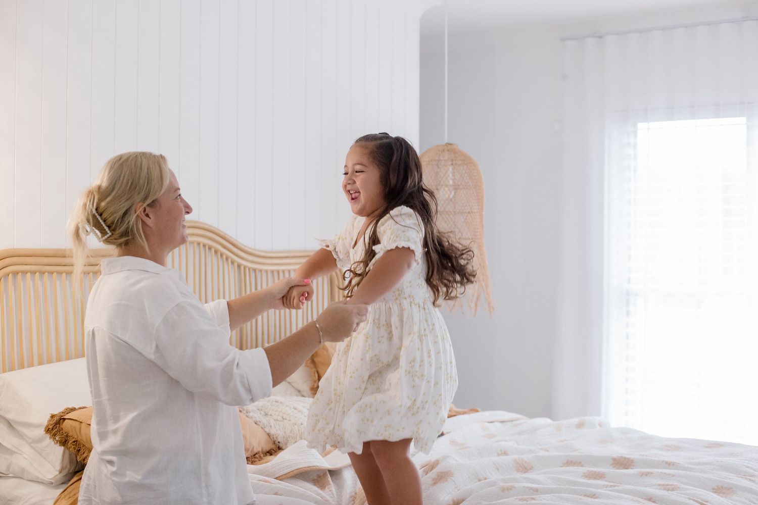 Playful moment captured between parent and child on beige upholstered bed.
