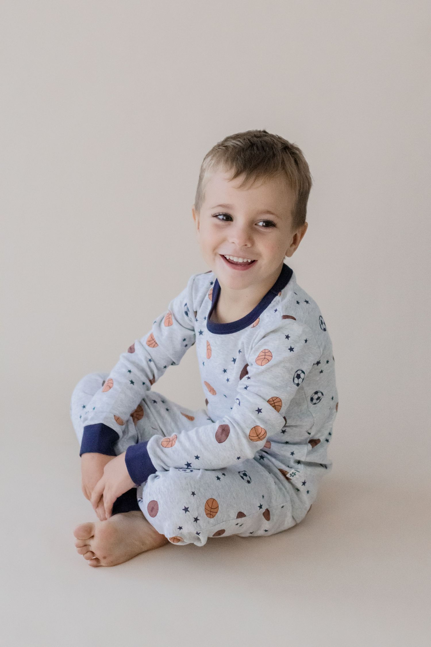 Child wearing space-themed pajamas sits cross-legged on beige background.