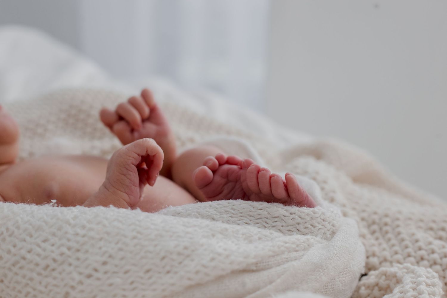 Tiny newborn baby feet peeking out from soft white knitted blanket in natural light.