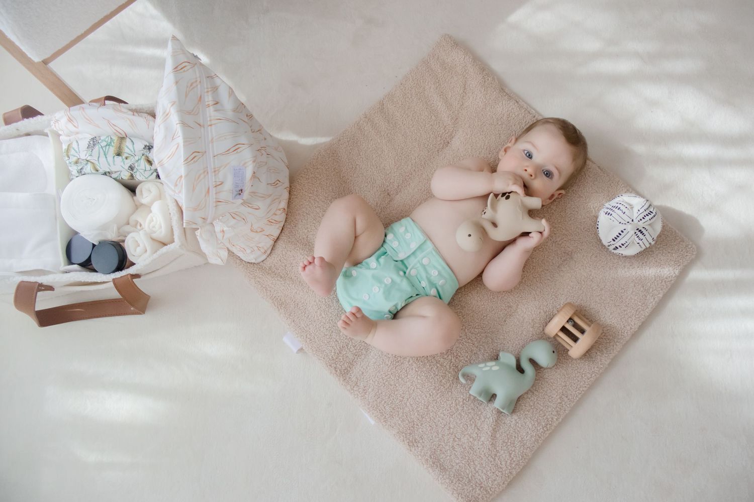 Baby essentials and soft toys arranged on neutral bedding with pastel accents.