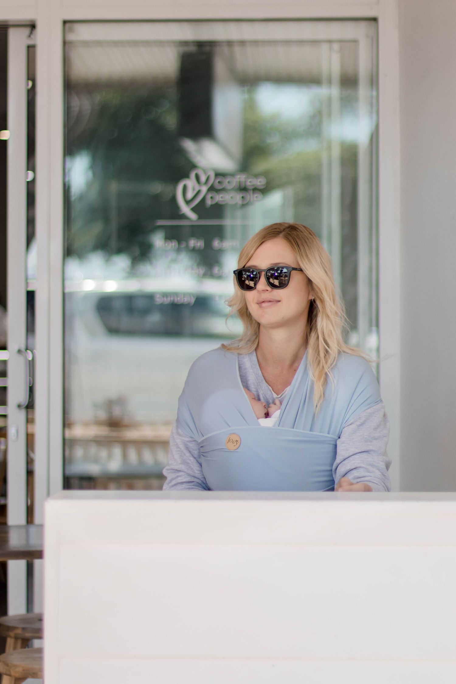 Woman in light blue button-up shirt and sunglasses sitting at outdoor patio area.