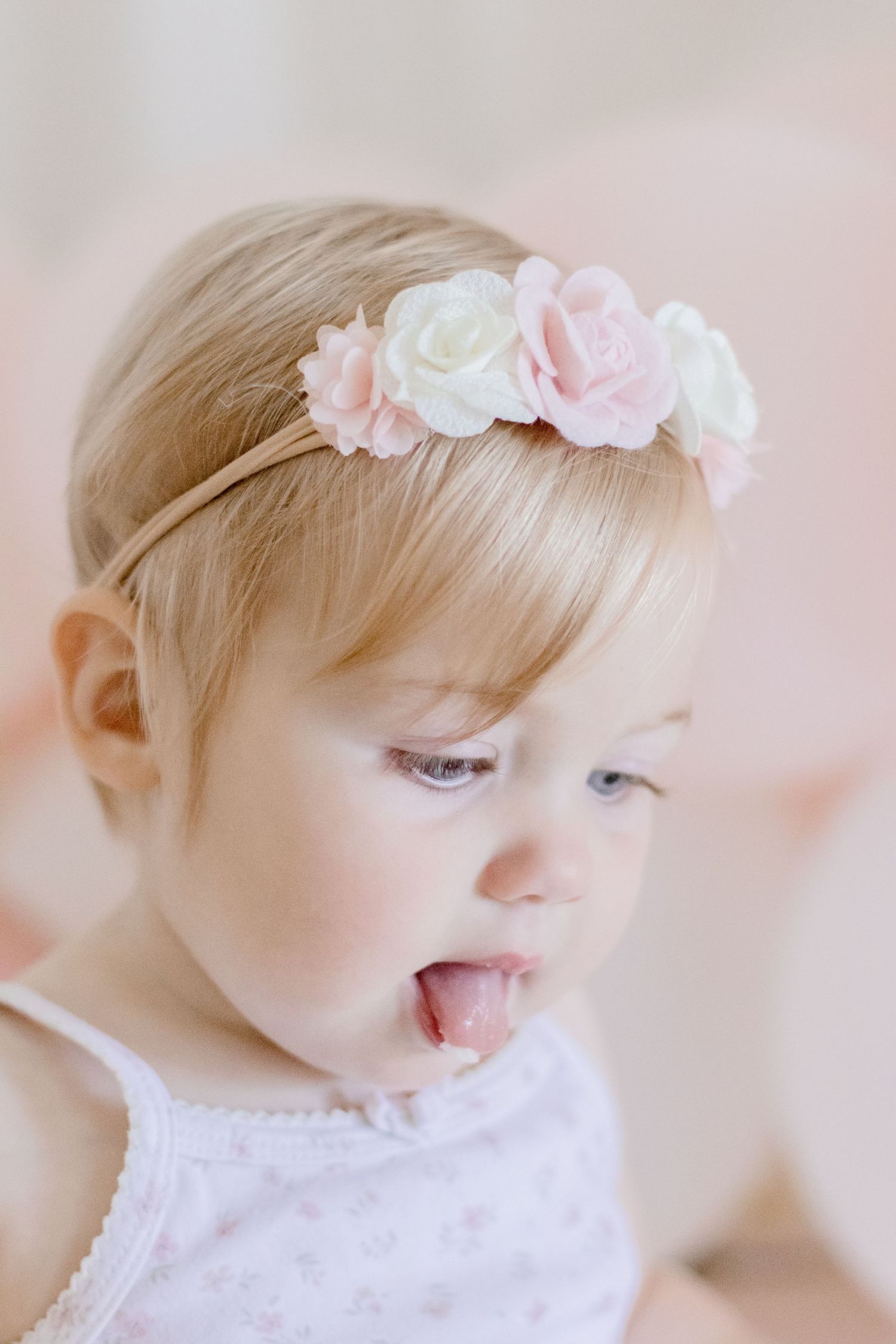 Baby with delicate floral headband looking down while wearing white lace dress.