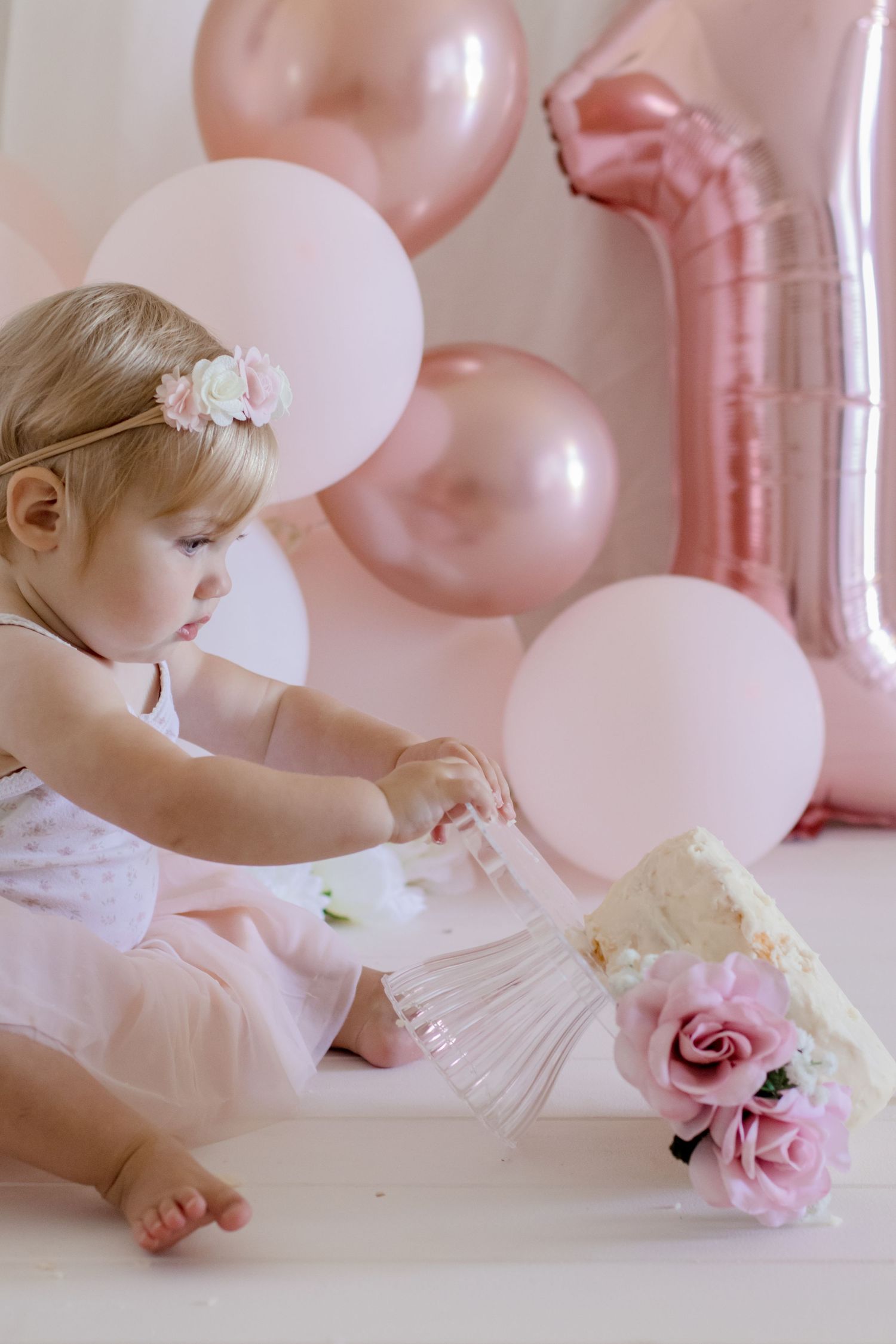 A delicate cake smash session with pink balloons and roses against a white backdrop.