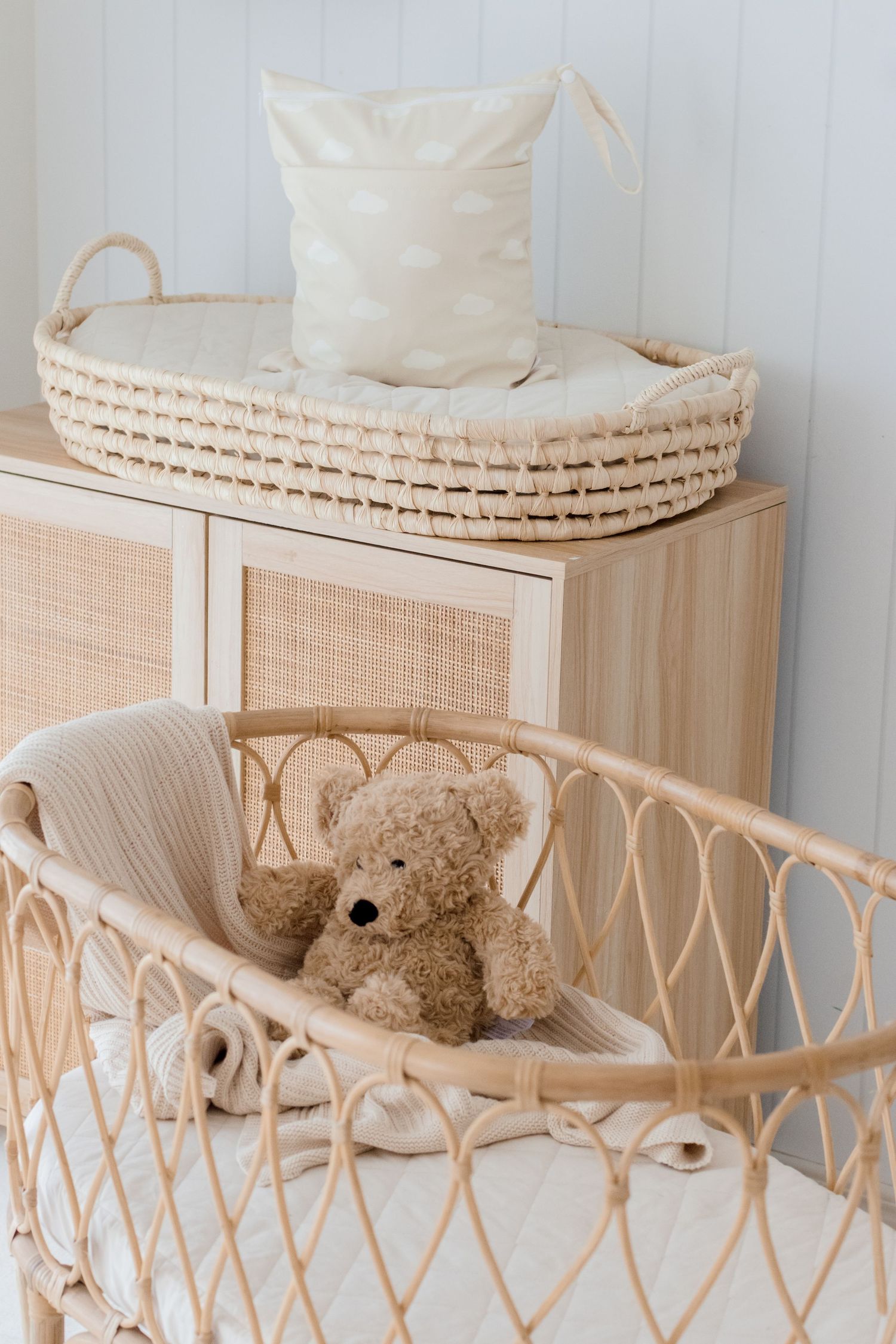 Cozy nursery corner with rattan bassinet, teddy bear, and woven storage baskets.