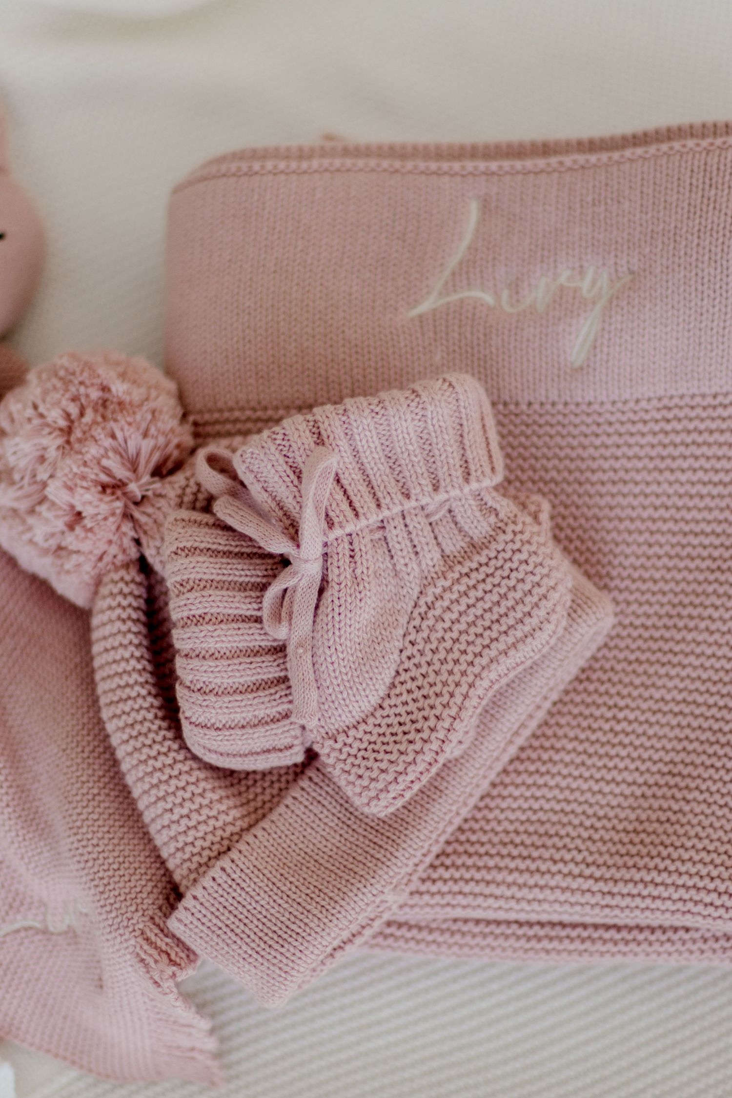 Soft pink knitted baby booties and blanket with decorative pom pom in pastel dusty rose color.