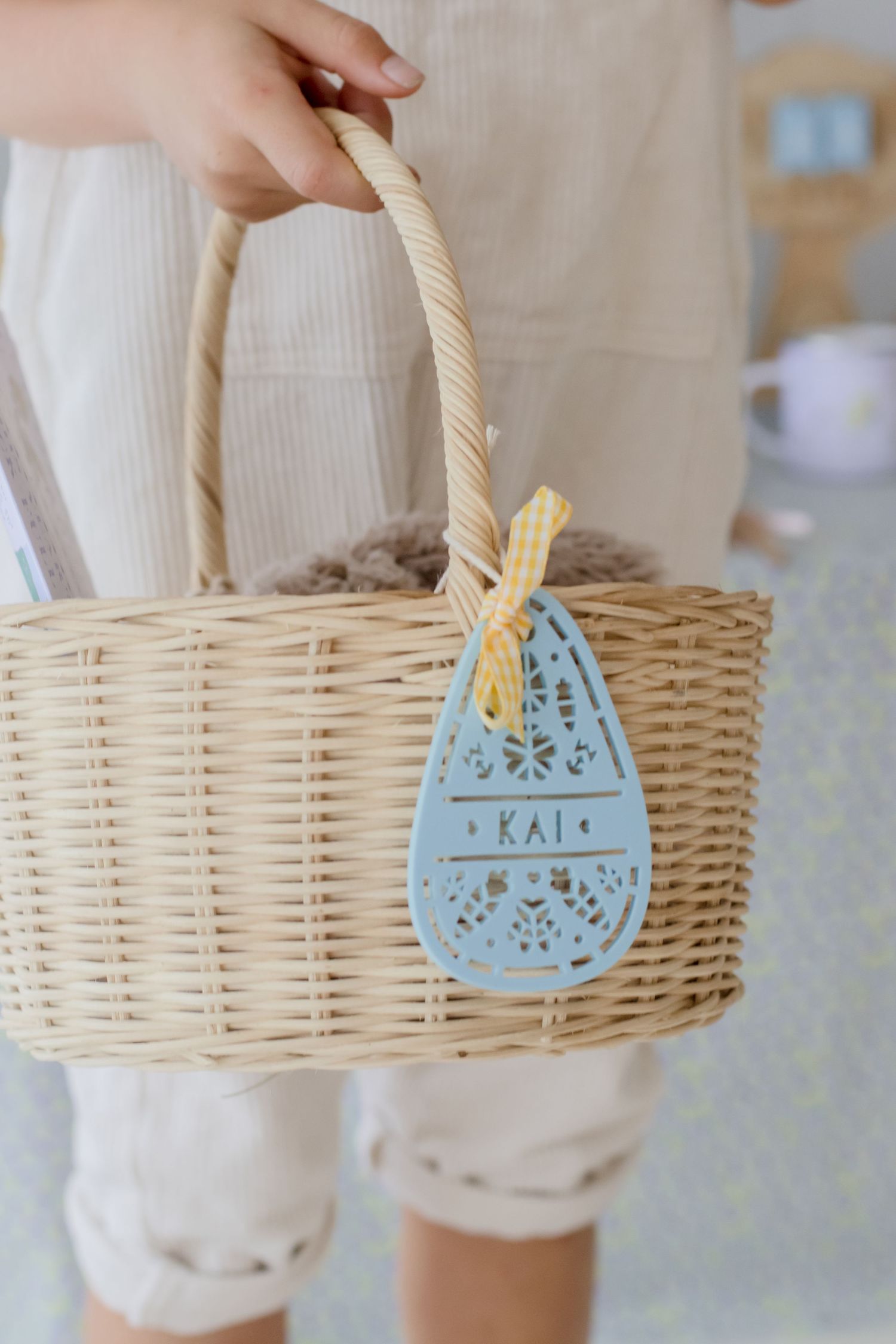 Woven basket with blue decorative tag reading 'Kai' being held by hand.
