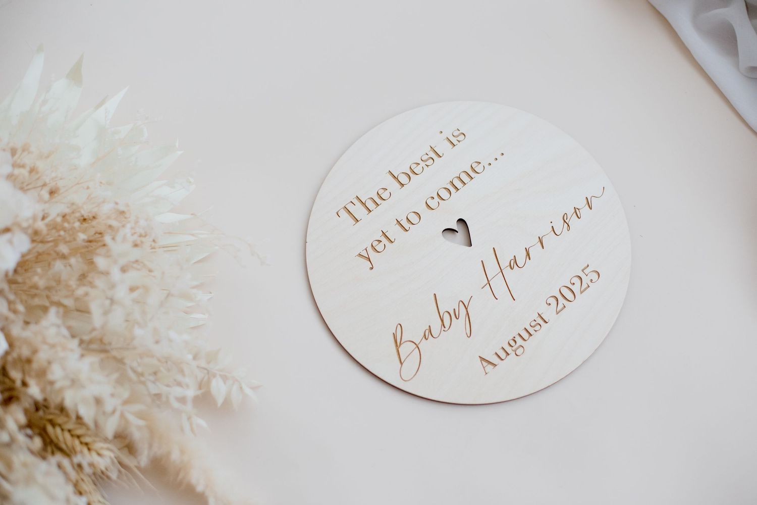 Round wooden pregnancy announcement sign with elegant script text.