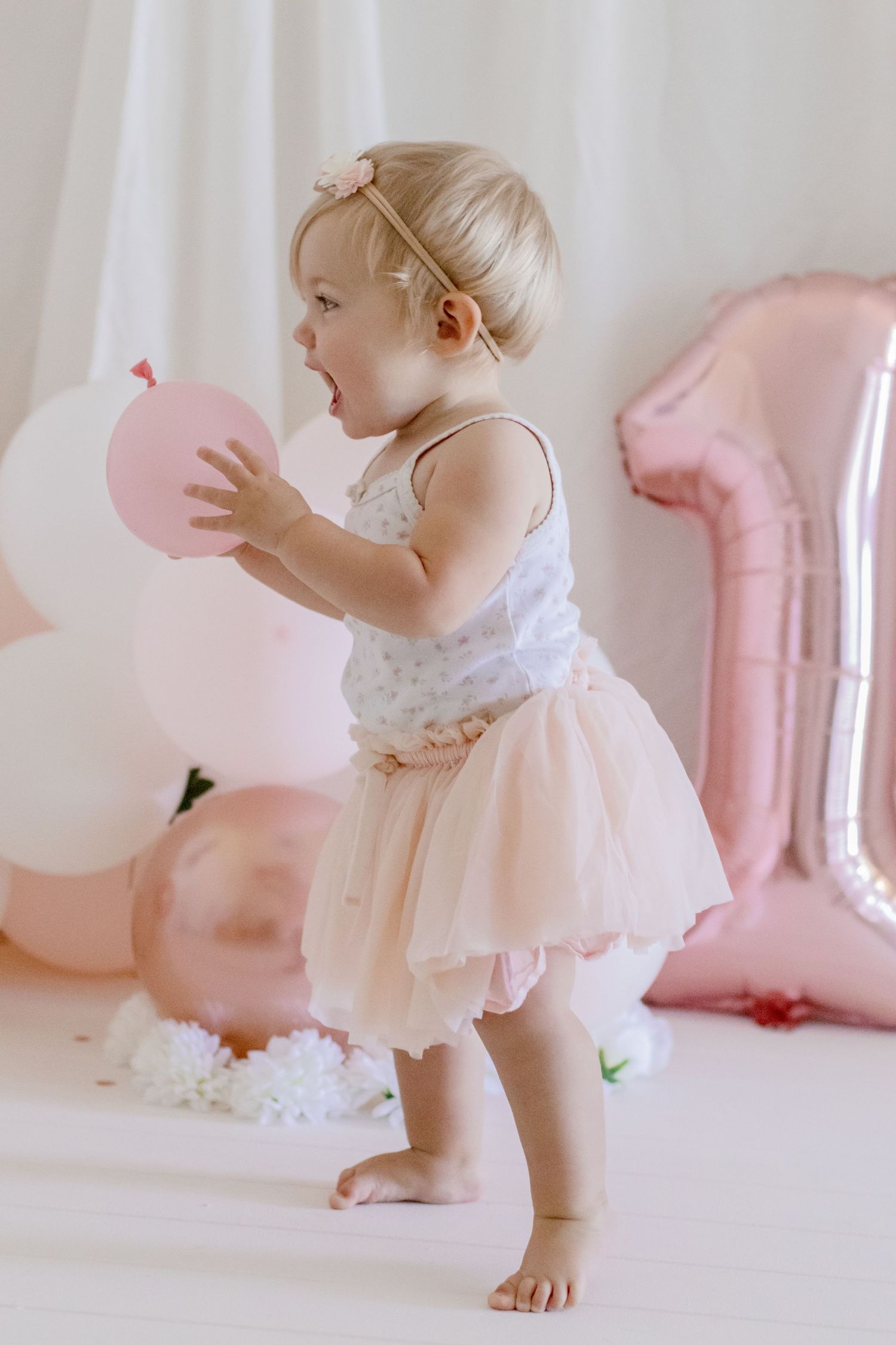 Toddler in ballet-inspired outfit plays with pink balloons during birthday photoshoot.
