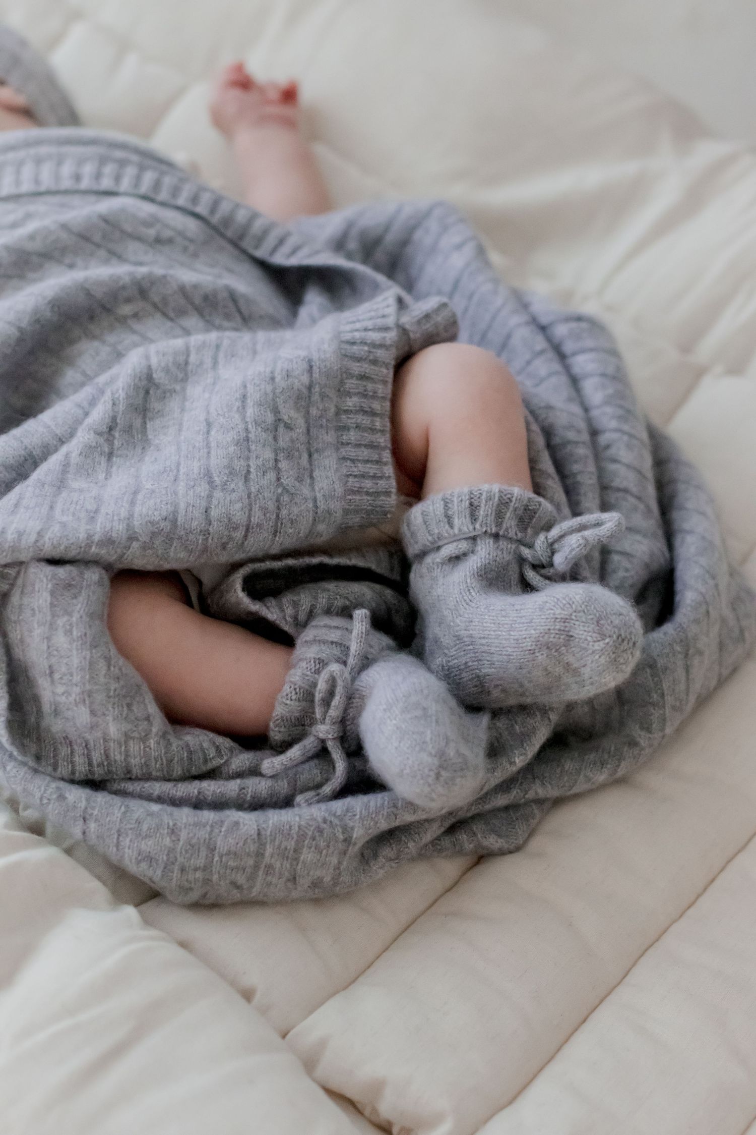 Step-by-step demonstration of folding a gray knit sweater by rolling it into a compact bundle on white bedding.