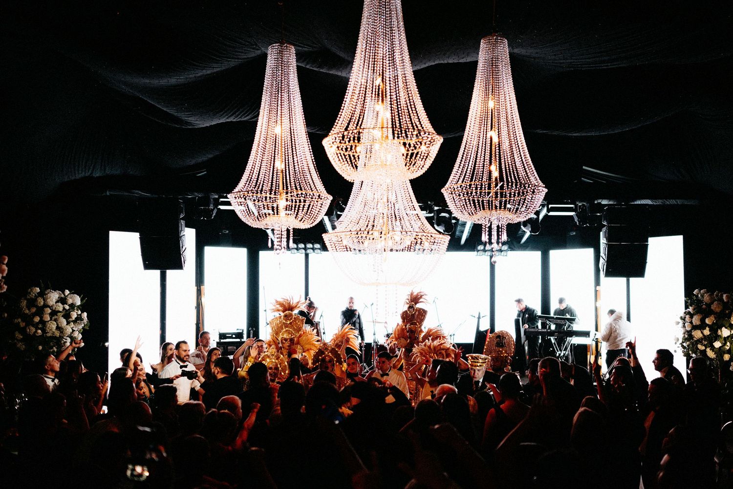 Crystal chandeliers illuminate a concert venue with a crowd silhouetted against bright stage lighting.