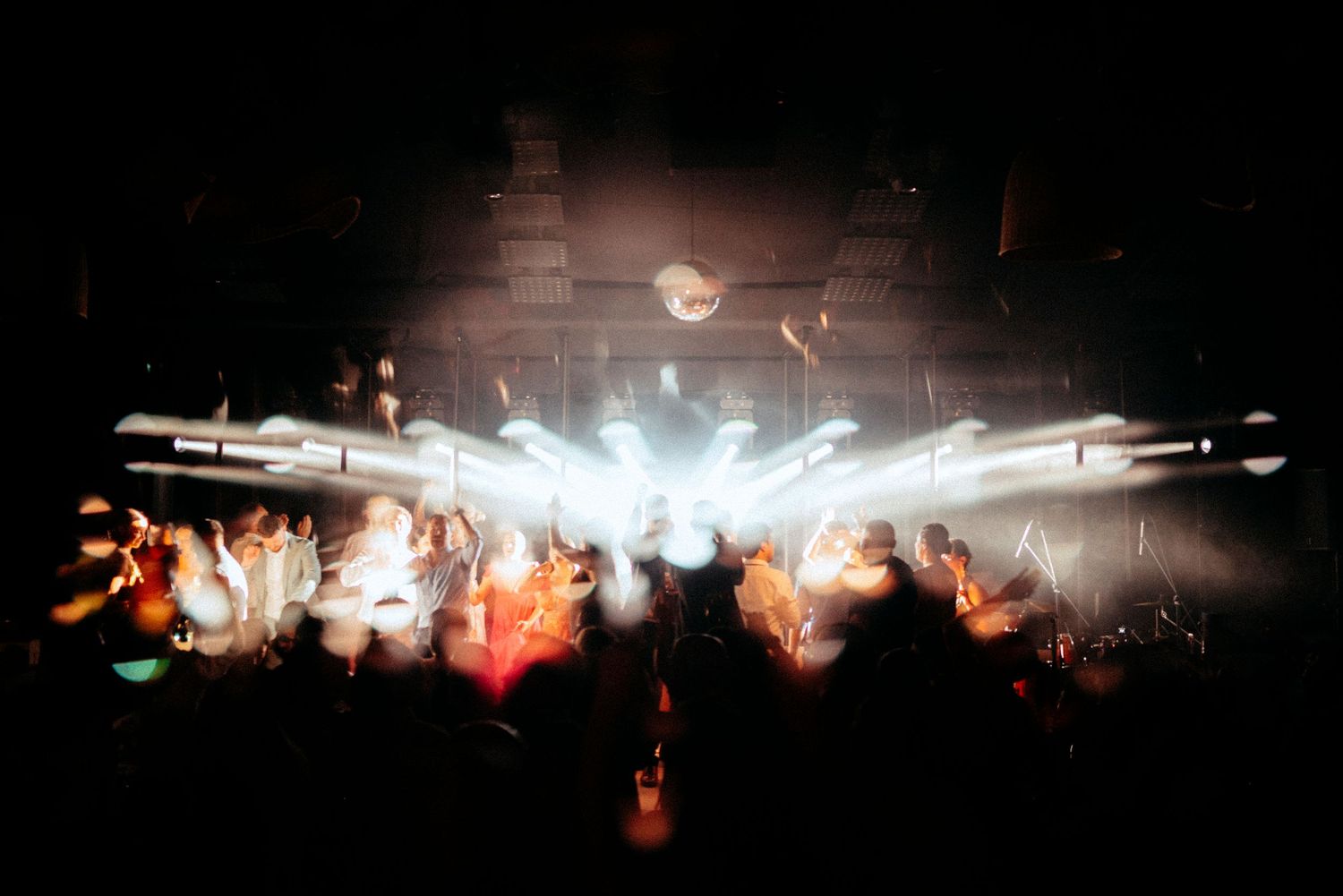 Crowd of wedding guests dance in dramatic white stage lighting and smoke at an electrifying indoor reception celebration.