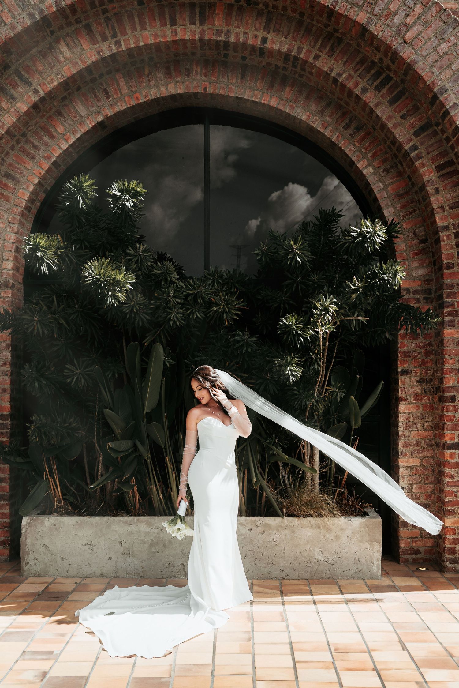 A sequence of artistic bridal photos showing flowing white wedding dress veil movement against a brick archway background.