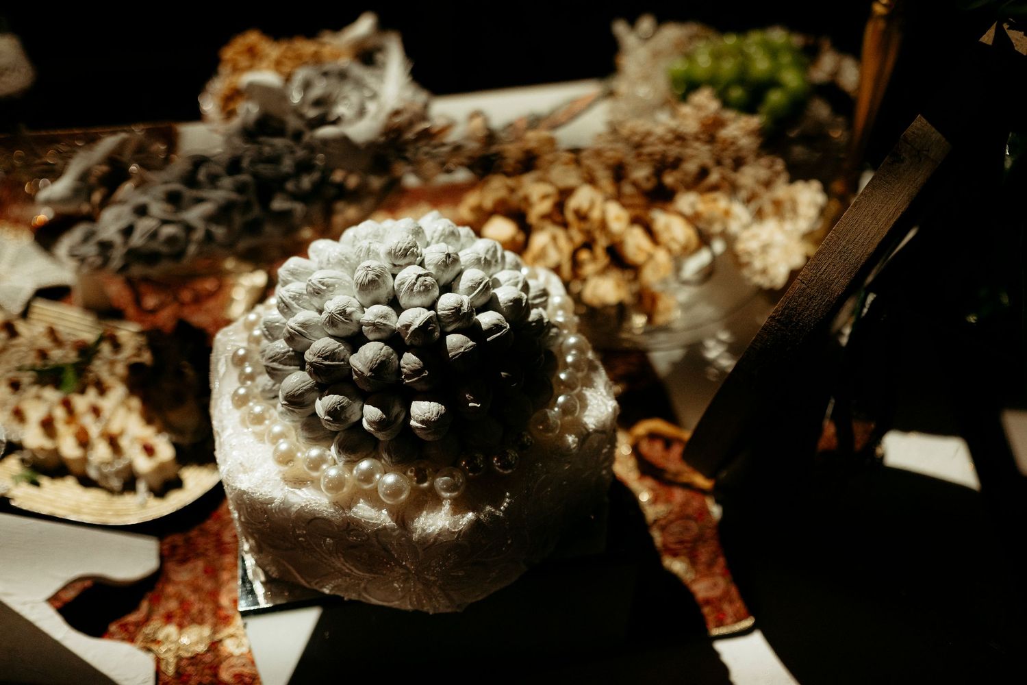 Elegant white wedding cake decorated with floral details surrounded by dessert table spread.