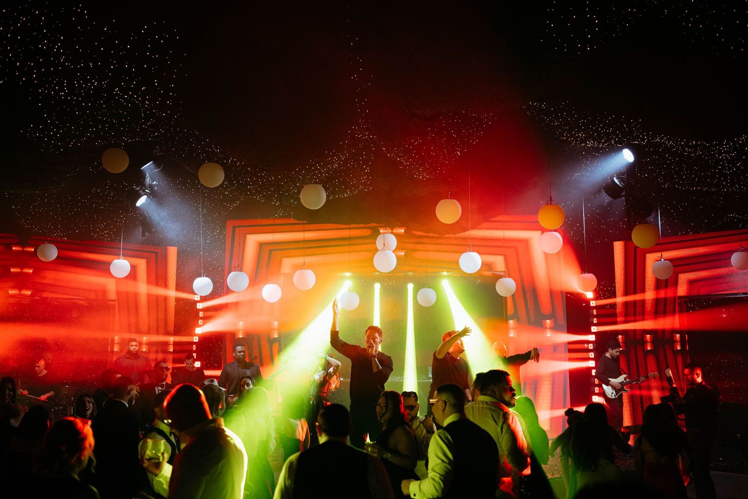 Crowd dancing at a vibrant nightclub with red and green laser lights illuminating a DJ stage.