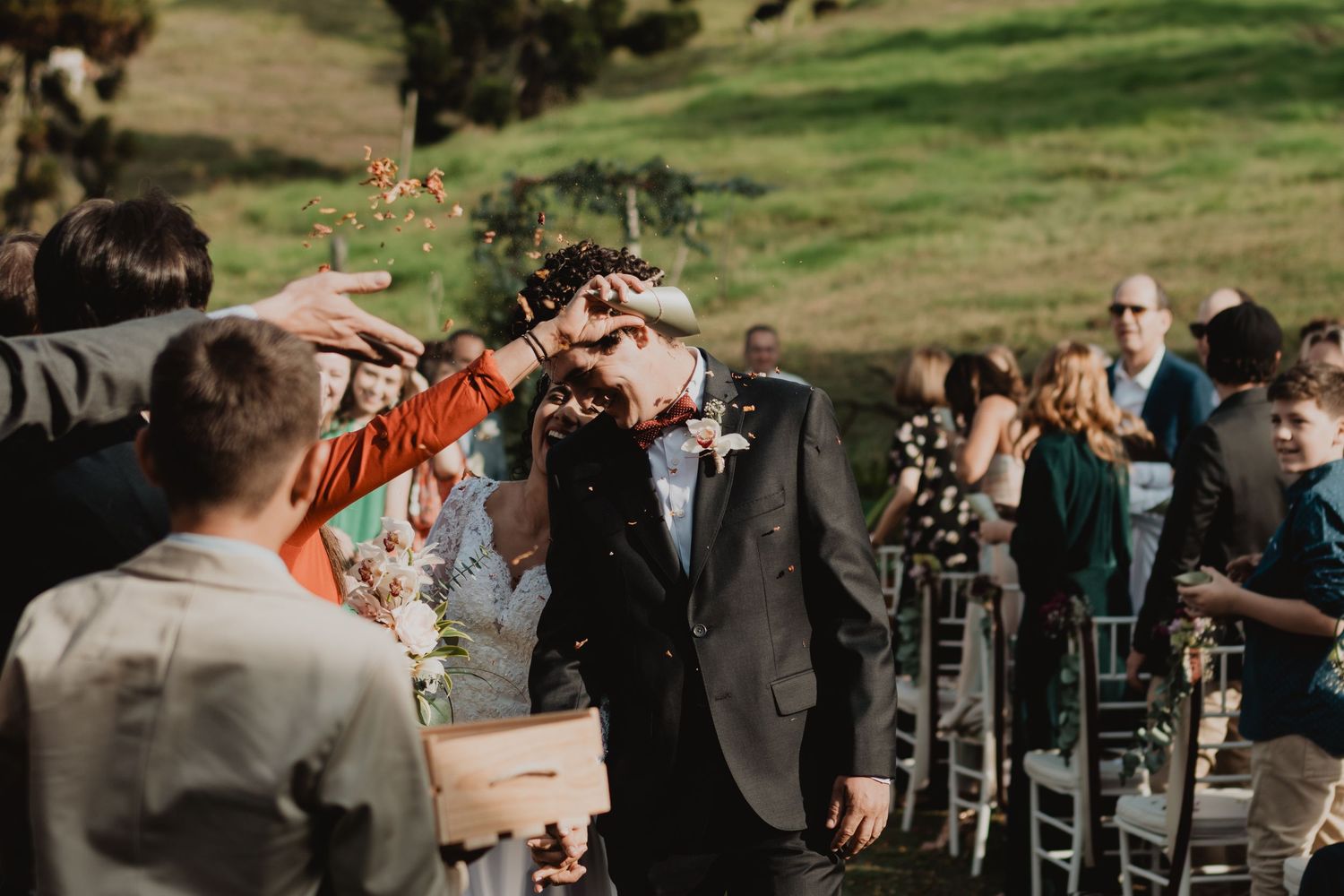 Newlywed couple walks down the aisle as guests toss flower petals at an outdoor wedding ceremony.