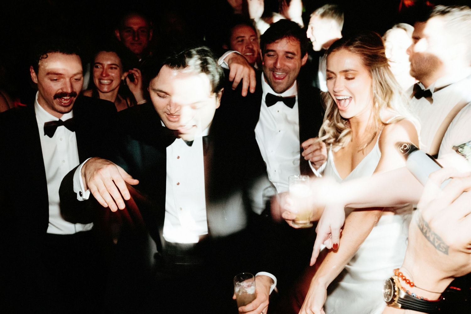Formal party scene with people dancing and celebrating in black tie attire.