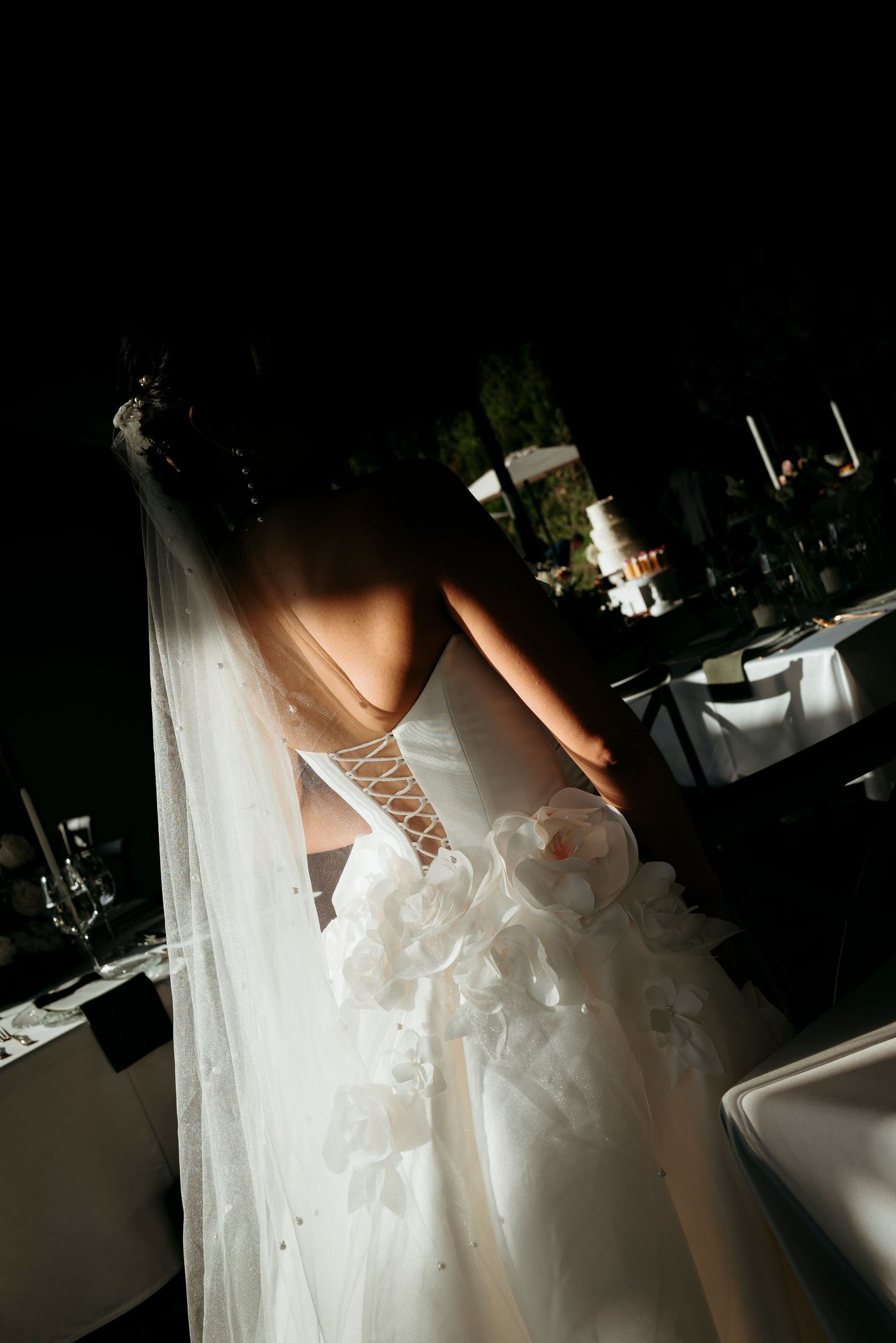 Close-up details of a white wedding dress with tulle and lace-up corset back in a dimly lit setting.