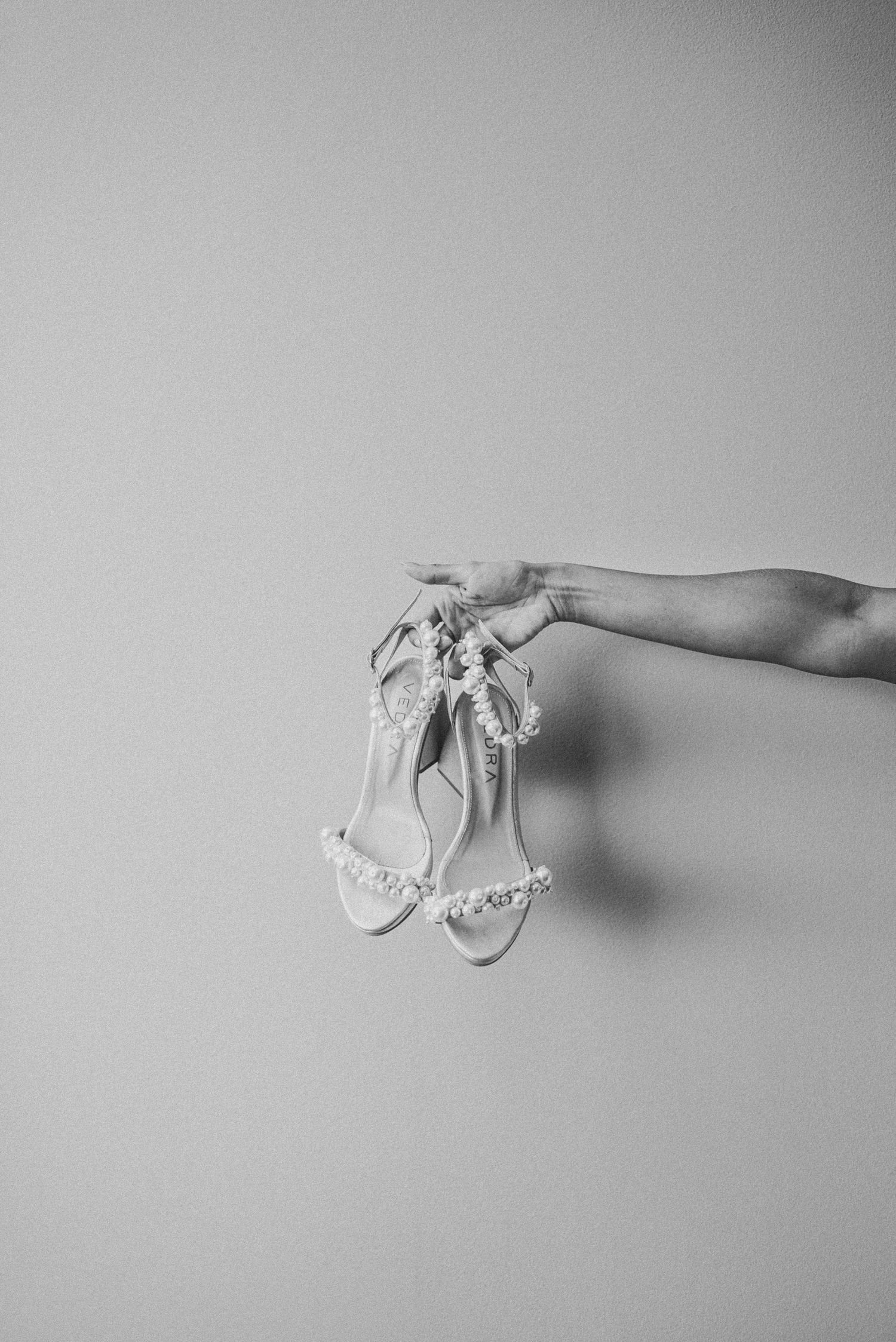 A minimalist black and white photo series showing a delicate white sandal being held against a light background.