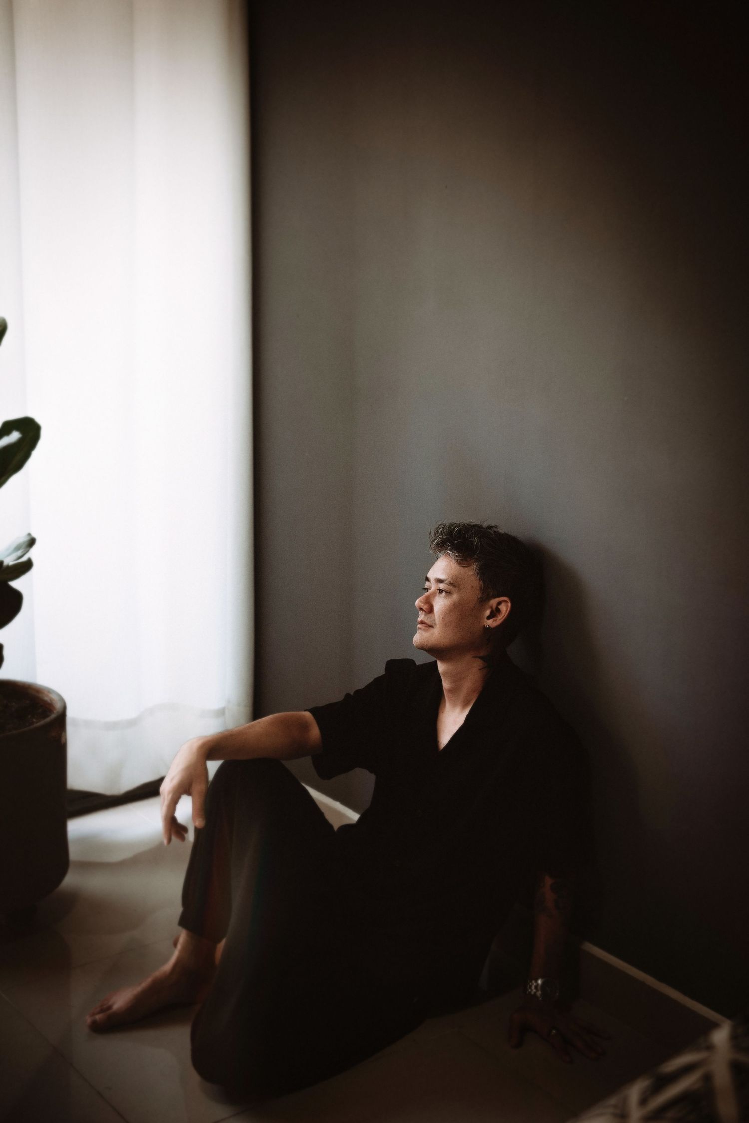 A series of moody photographs shows a figure in dark clothing sitting against a white wall in different positions.