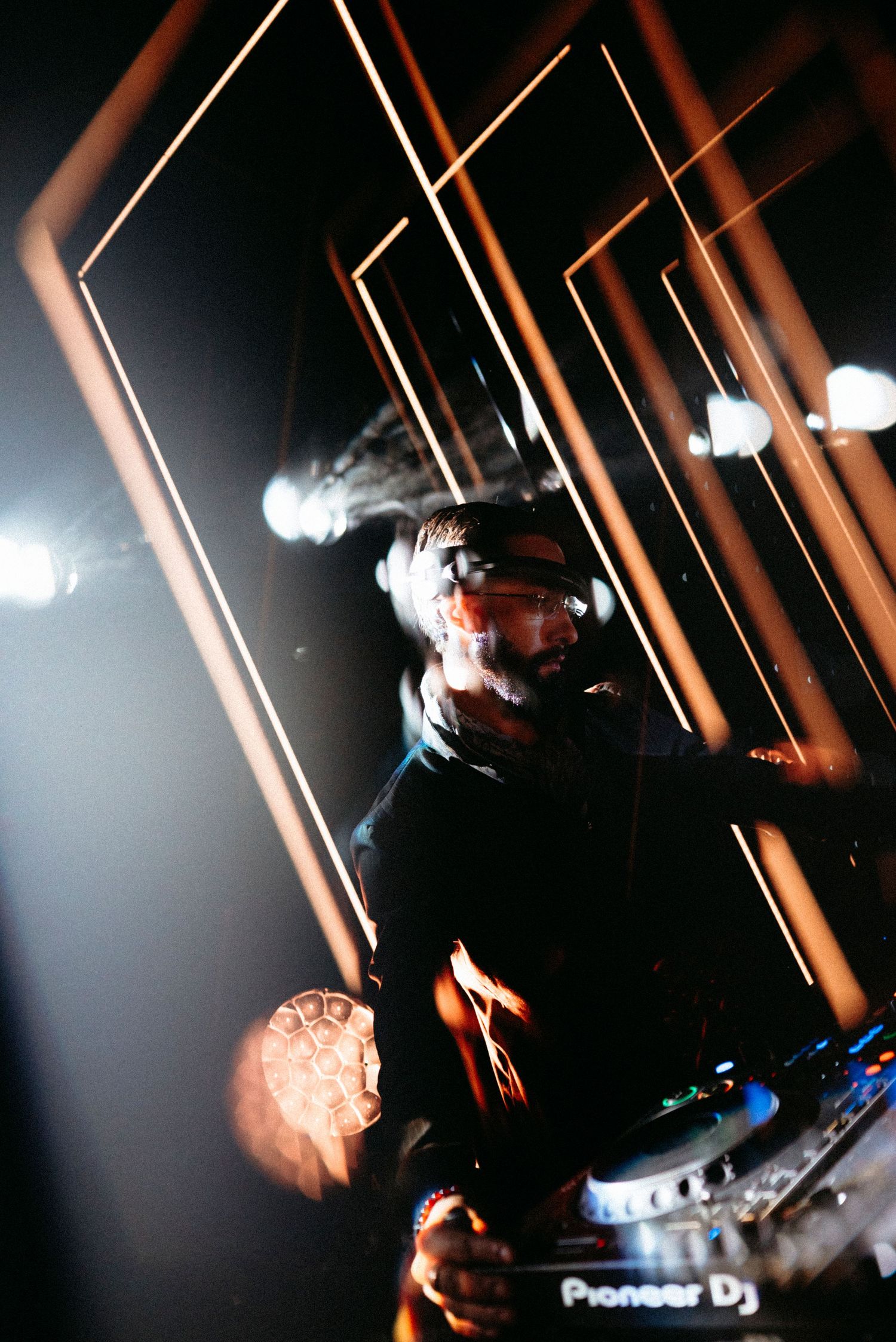 DJ performing at a nightclub using Pioneer DJ equipment surrounded by geometric golden light installations.