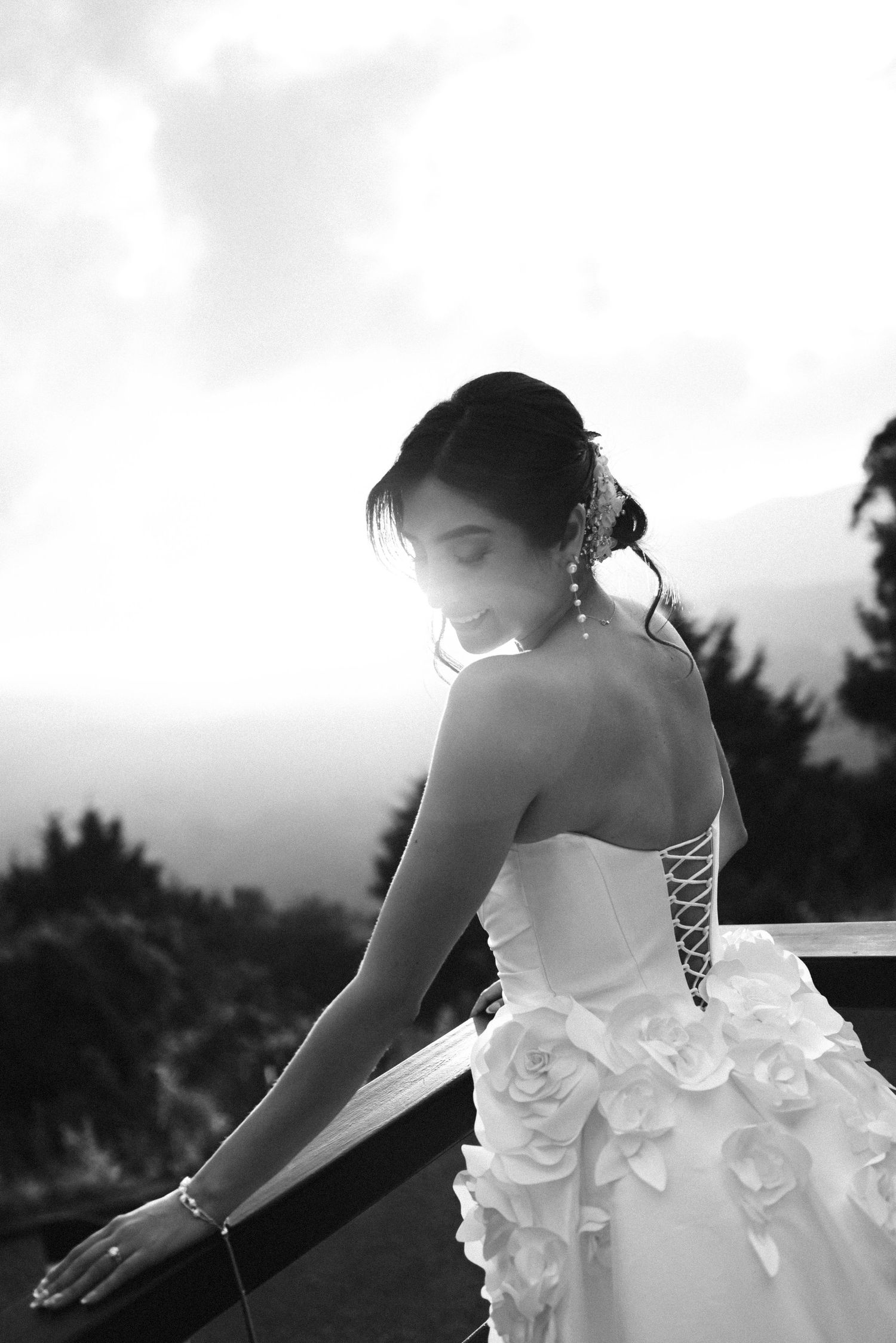 A bride in a white strapless wedding dress with floral details poses in an artistic black and white photo series.