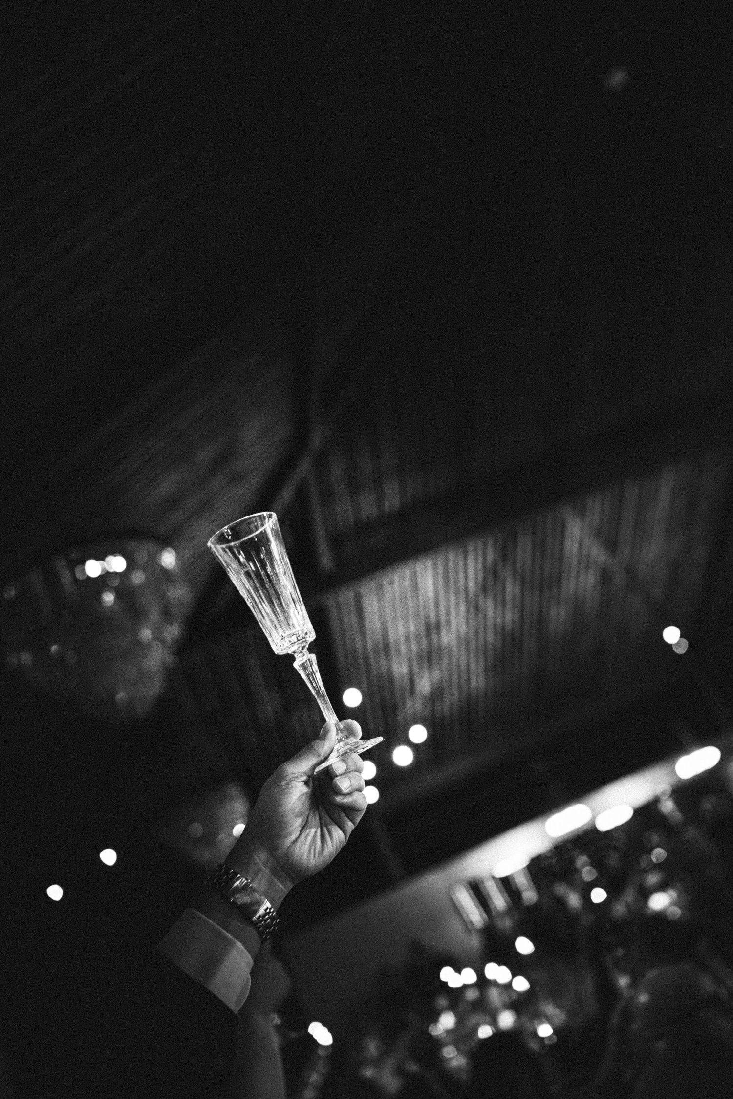 Black and white photo of hand raising crystal champagne flute in wedding toast celebration.