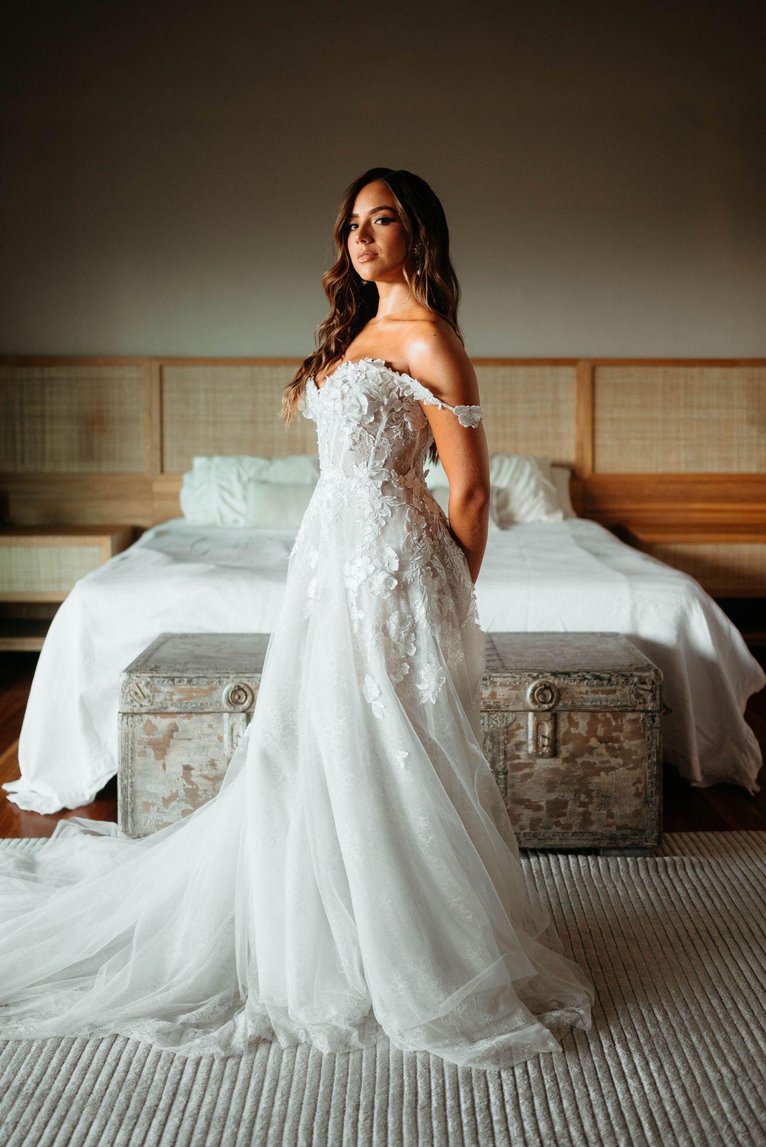 A stunning white wedding dress with intricate lace details and flowing tulle skirt spreads elegantly across a carpeted floor.