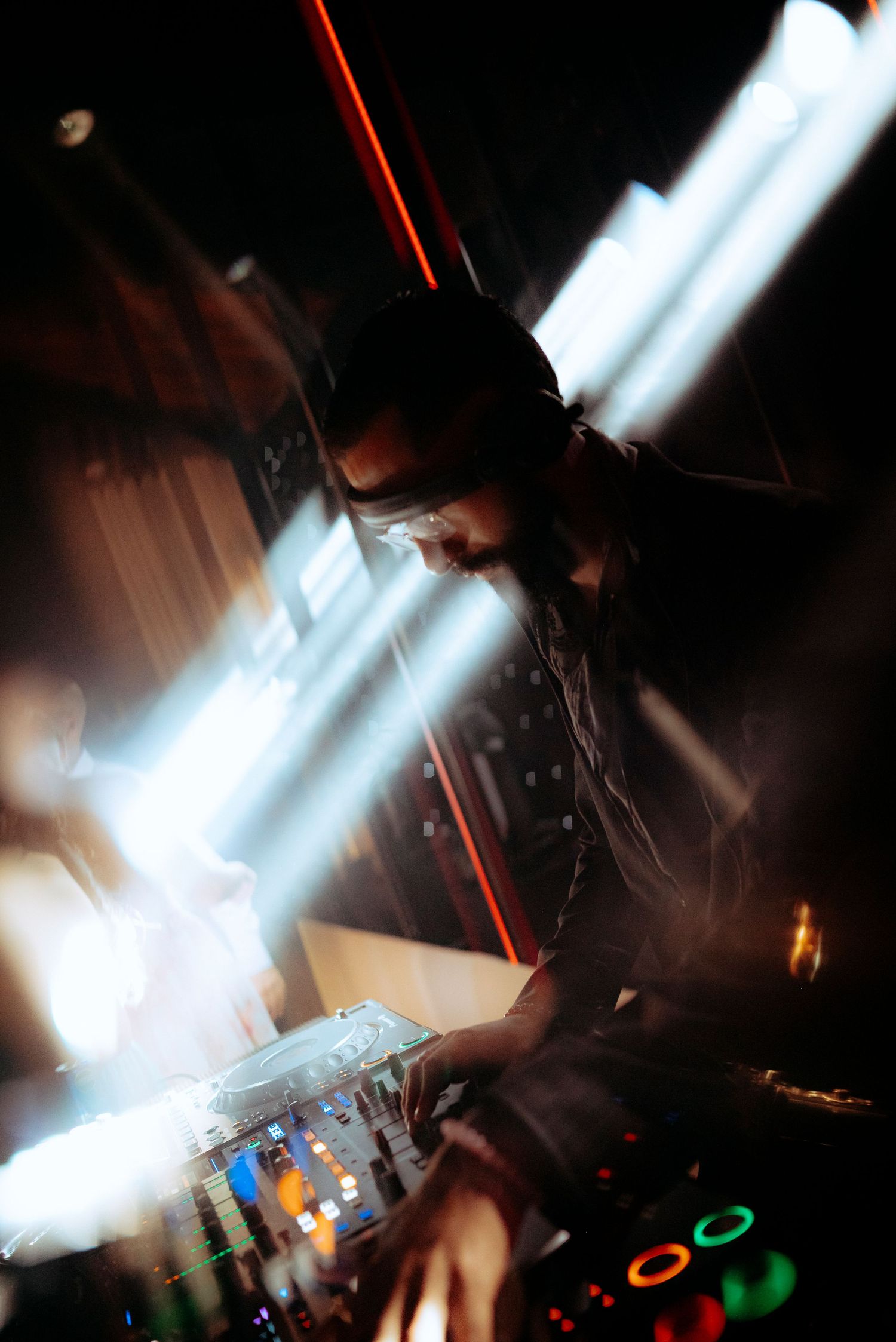 DJ performing at night club with dramatic light beams illuminating the mixing console.
