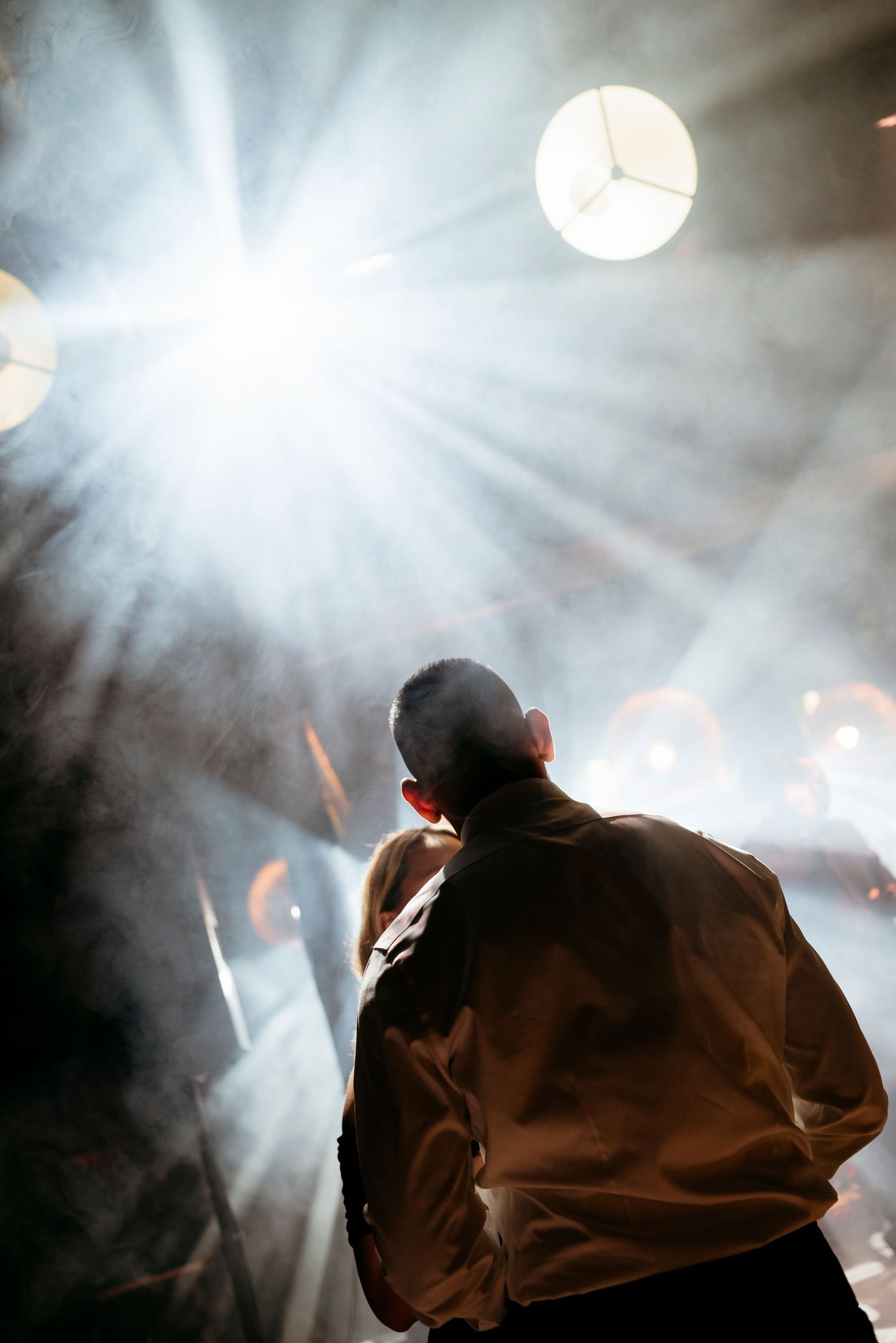 Silhouetted couple dancing under a bright spotlight with dramatic rays of light and smoke effects.