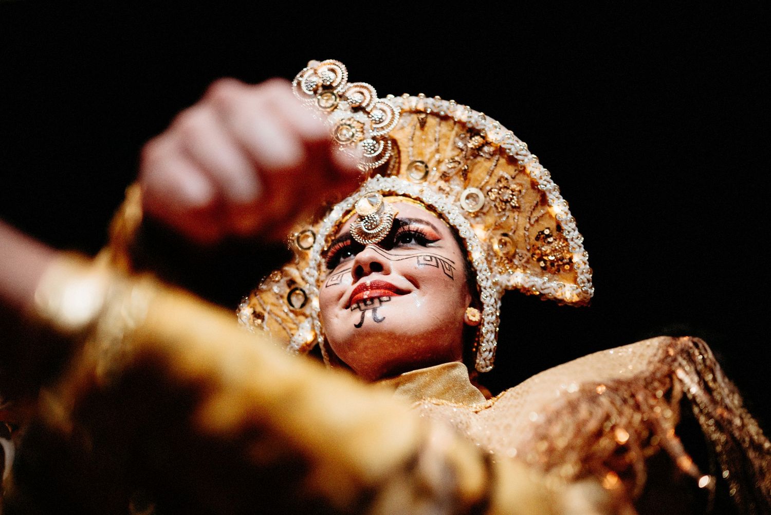 Traditional performer in ornate gold headdress and dramatic makeup during a cultural dance performance.