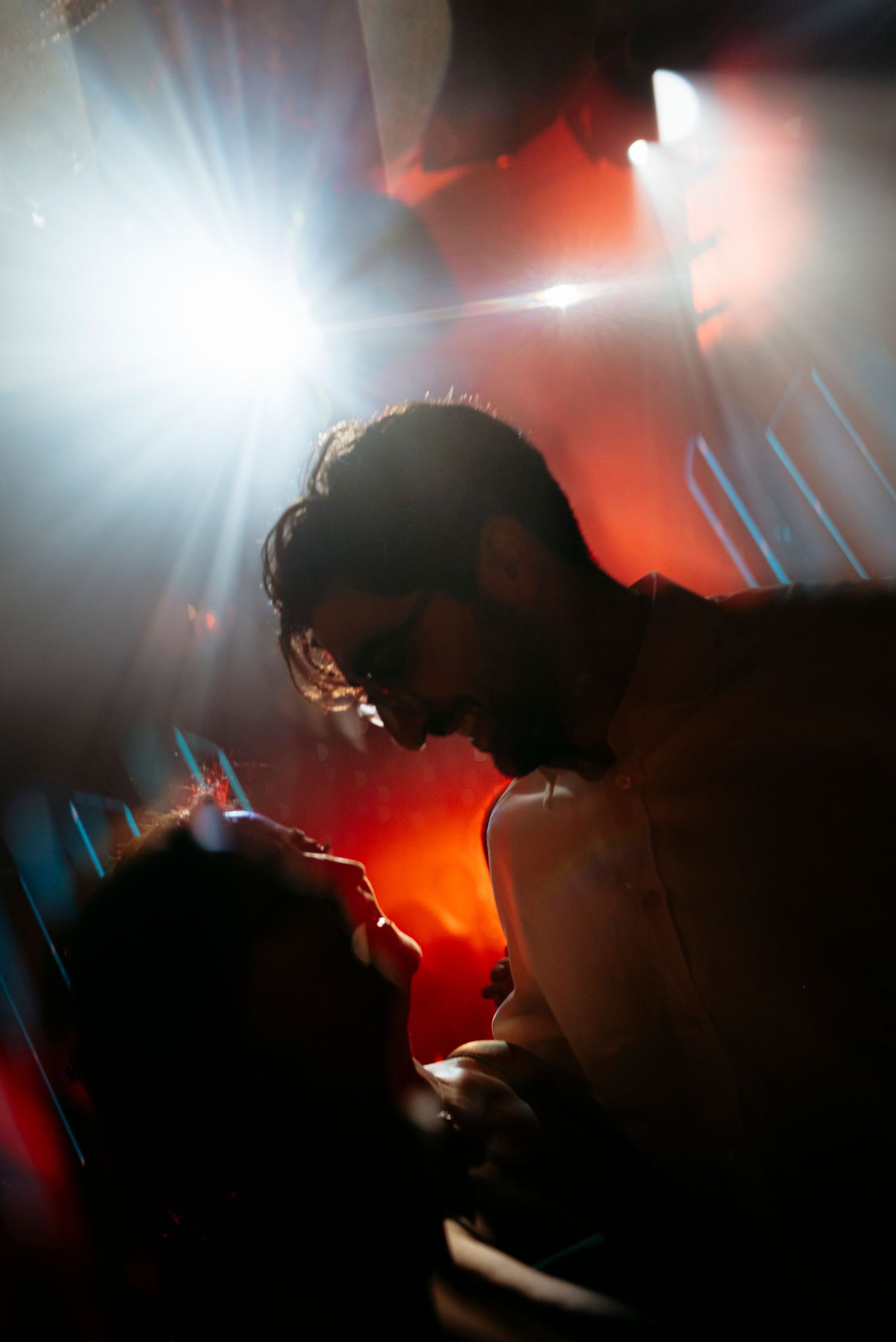 Dramatic silhouette of bride and groom sharing an intimate moment with colorful stage lights behind them.