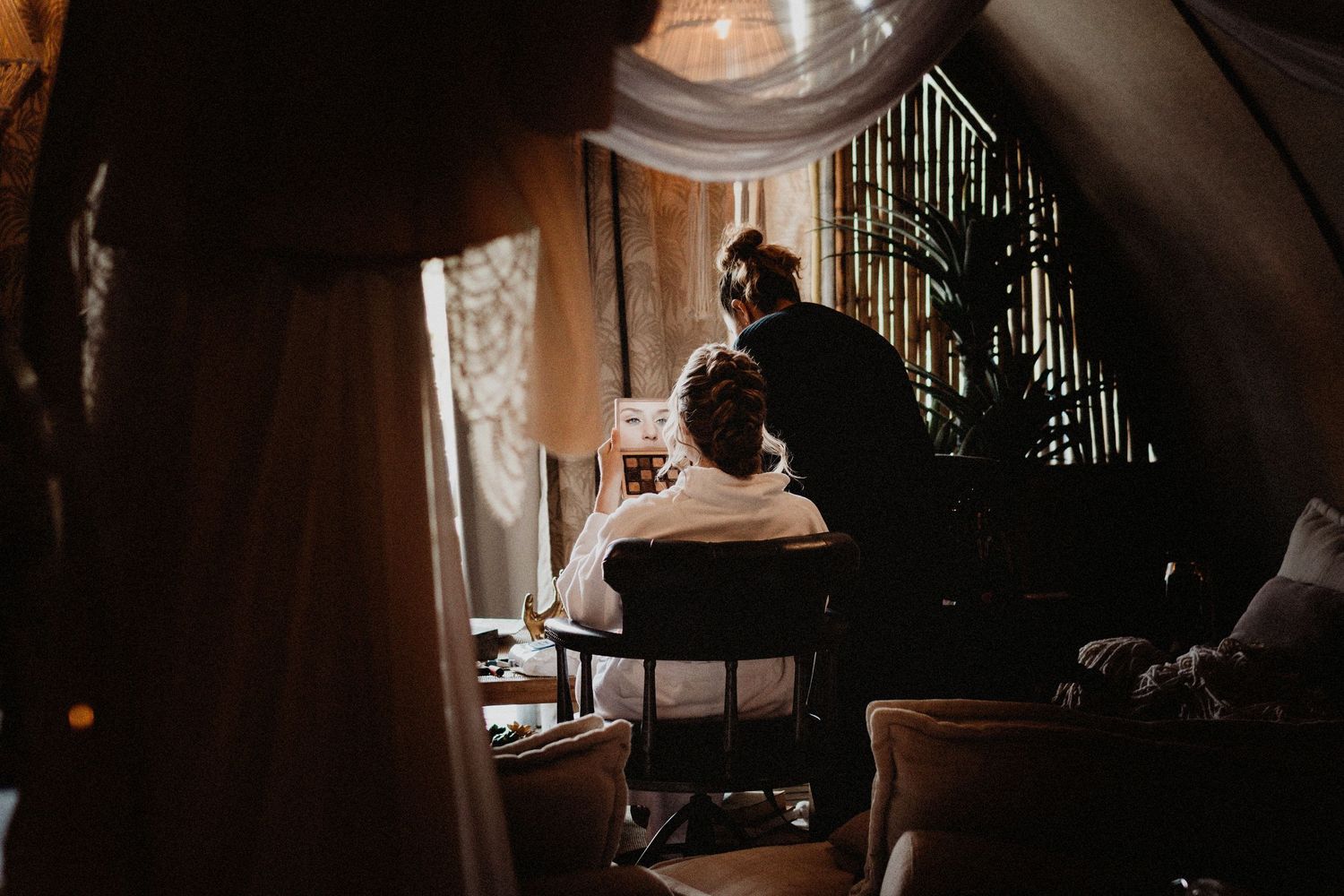 Silhouetted figure sits by window in dimly lit room creating moody artistic atmosphere.