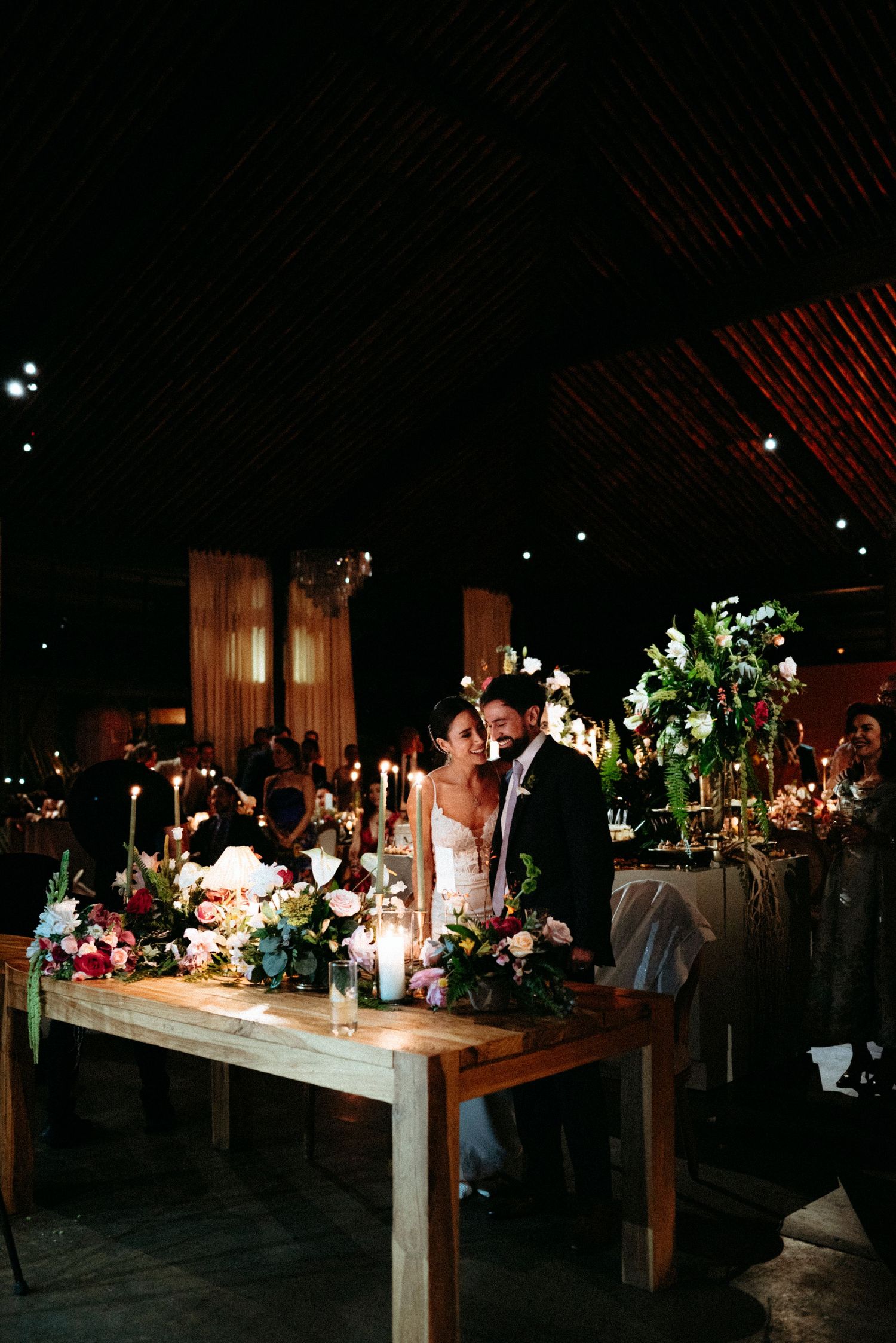Bride and groom share a romantic moment at their candlelit floral wedding reception table in a rustic barn venue.