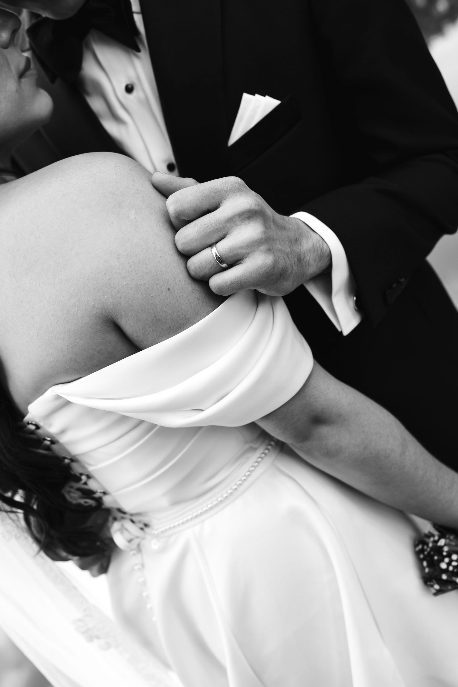 Black and white close-up of a couple dancing at a wedding, showing formal attire and an intimate embrace.