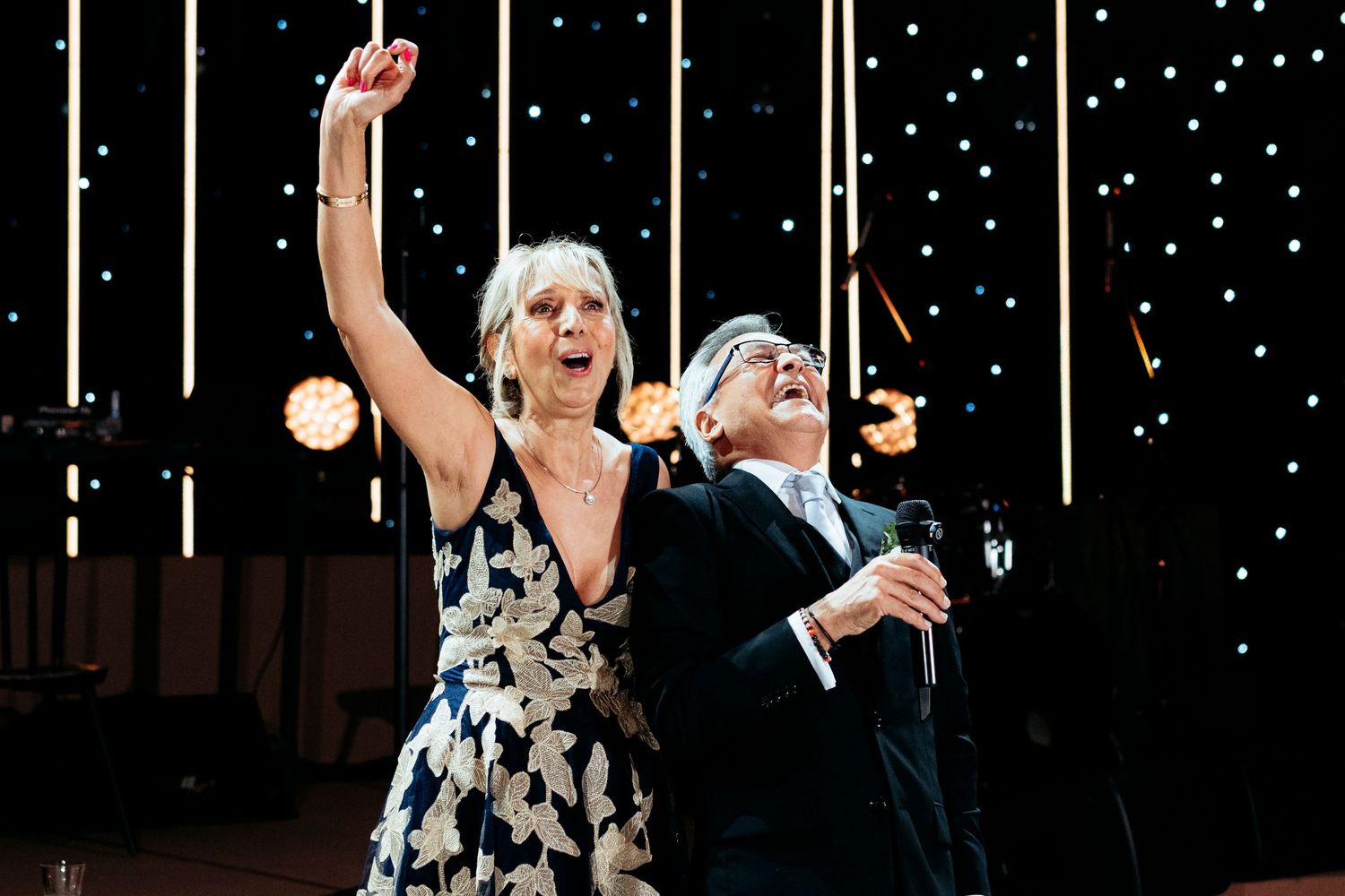 Two joyful guests dancing and celebrating at an elegant wedding reception with twinkling lights backdrop.
