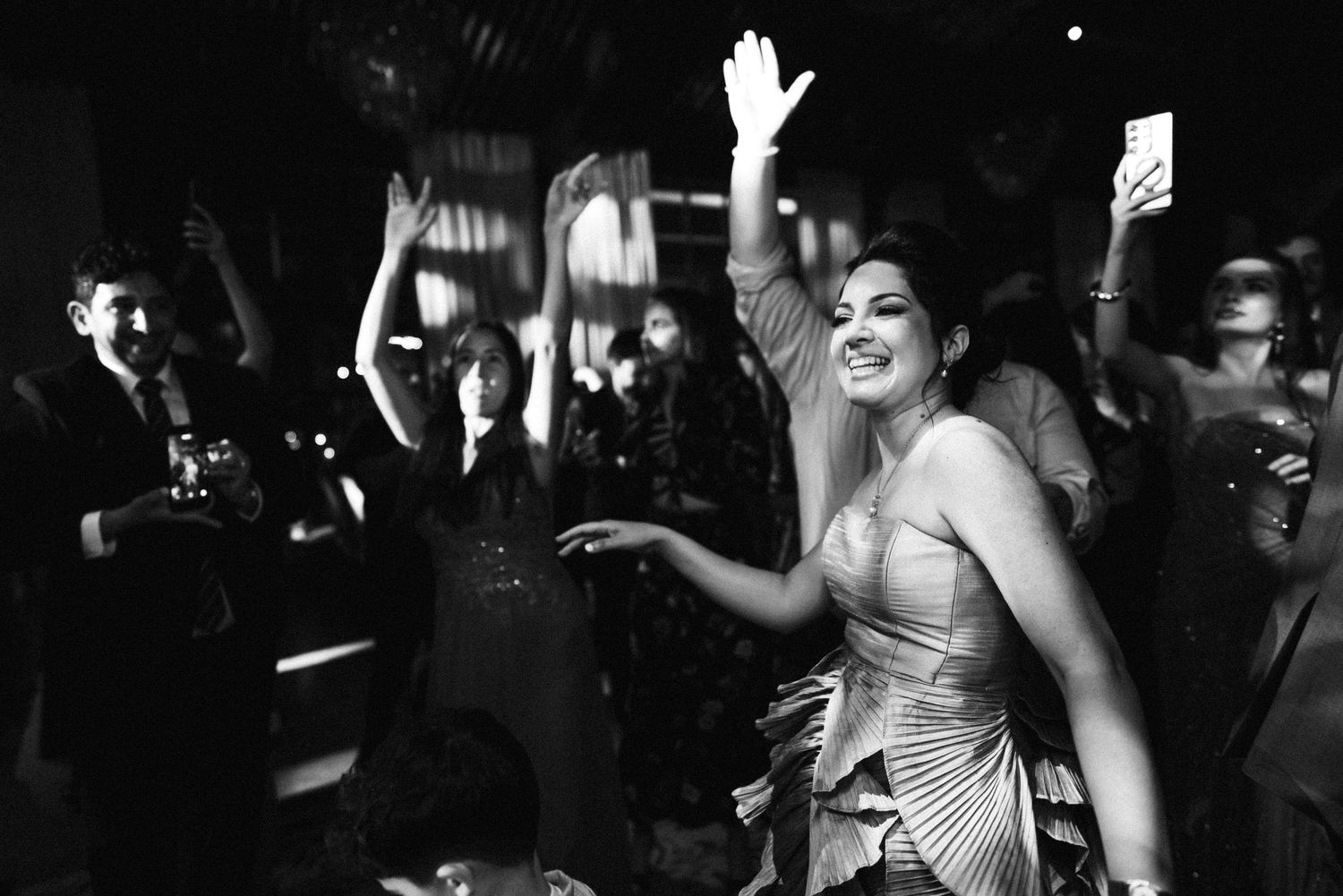 Guest in silver dress dances joyfully at black and white wedding reception party.