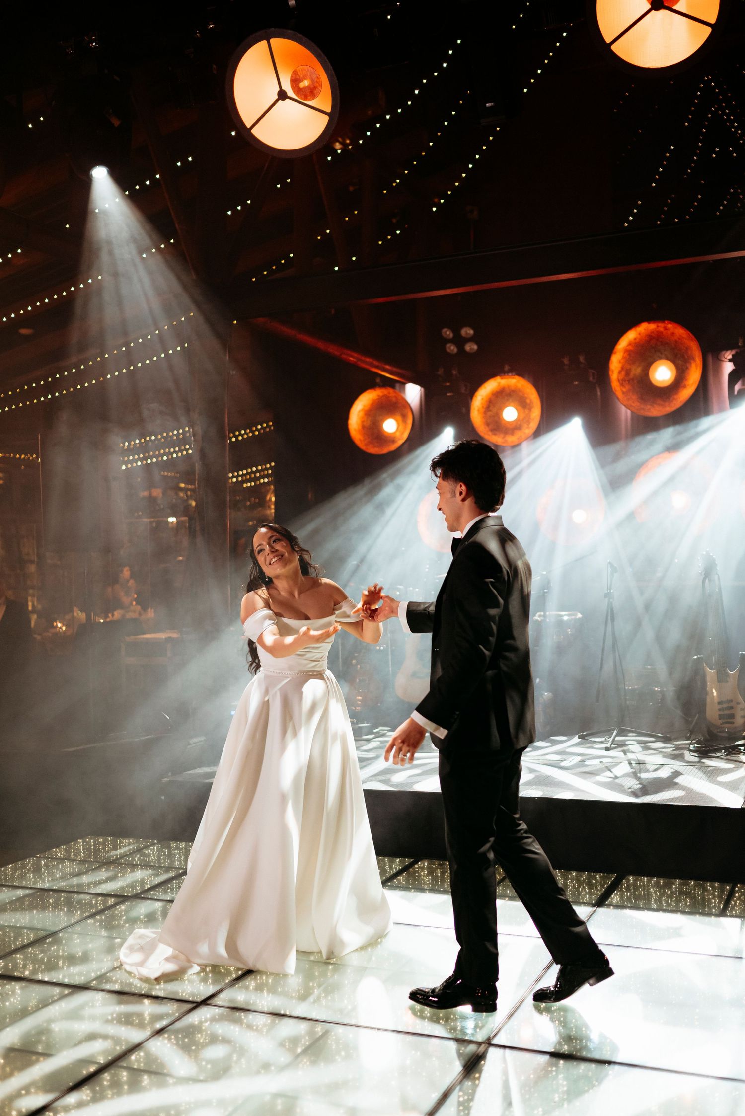 Bride and groom sharing their first dance on a mirrored floor under dramatic wedding lights.