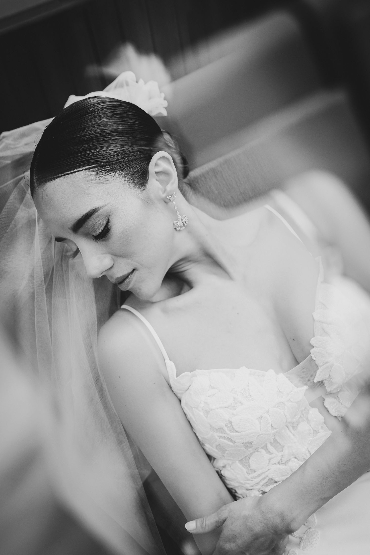 Black and white photo of a bride in a floral wedding dress and veil, looking down gracefully on her wedding day.