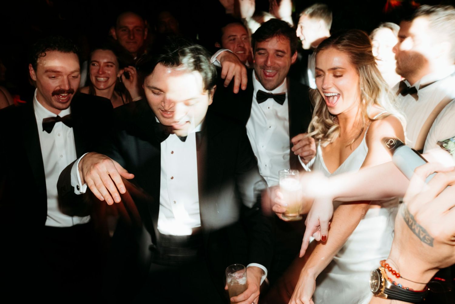 People in formal attire dancing and celebrating at an elegant evening party with tuxedos and evening gowns.