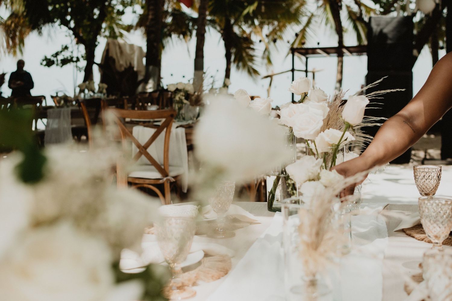 A rustic wedding reception table setting with soft pink floral arrangements and delicate glassware in natural lighting.